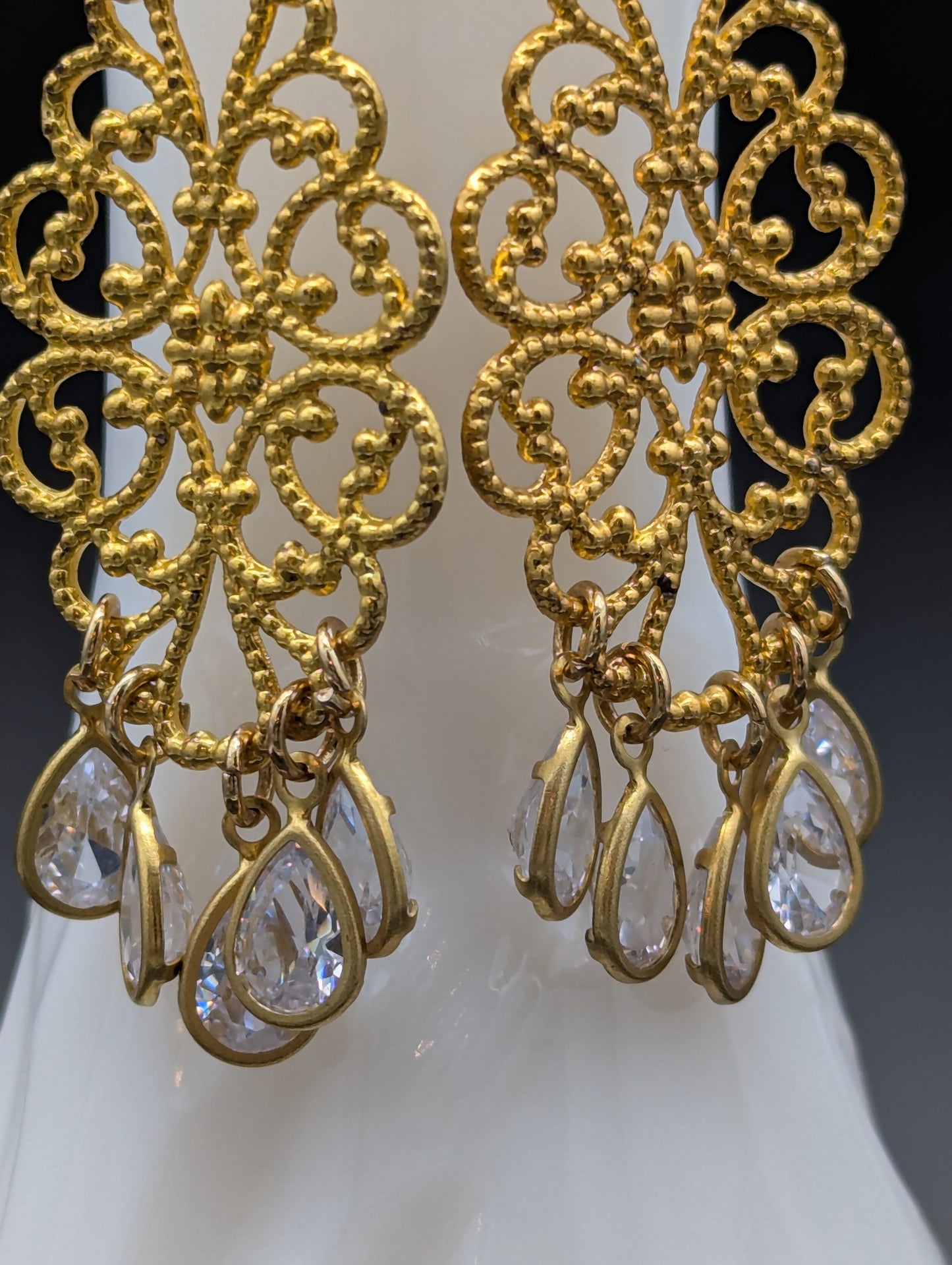 Close-up of a set of golden filigree earrings with teardrop-shaped crystals.