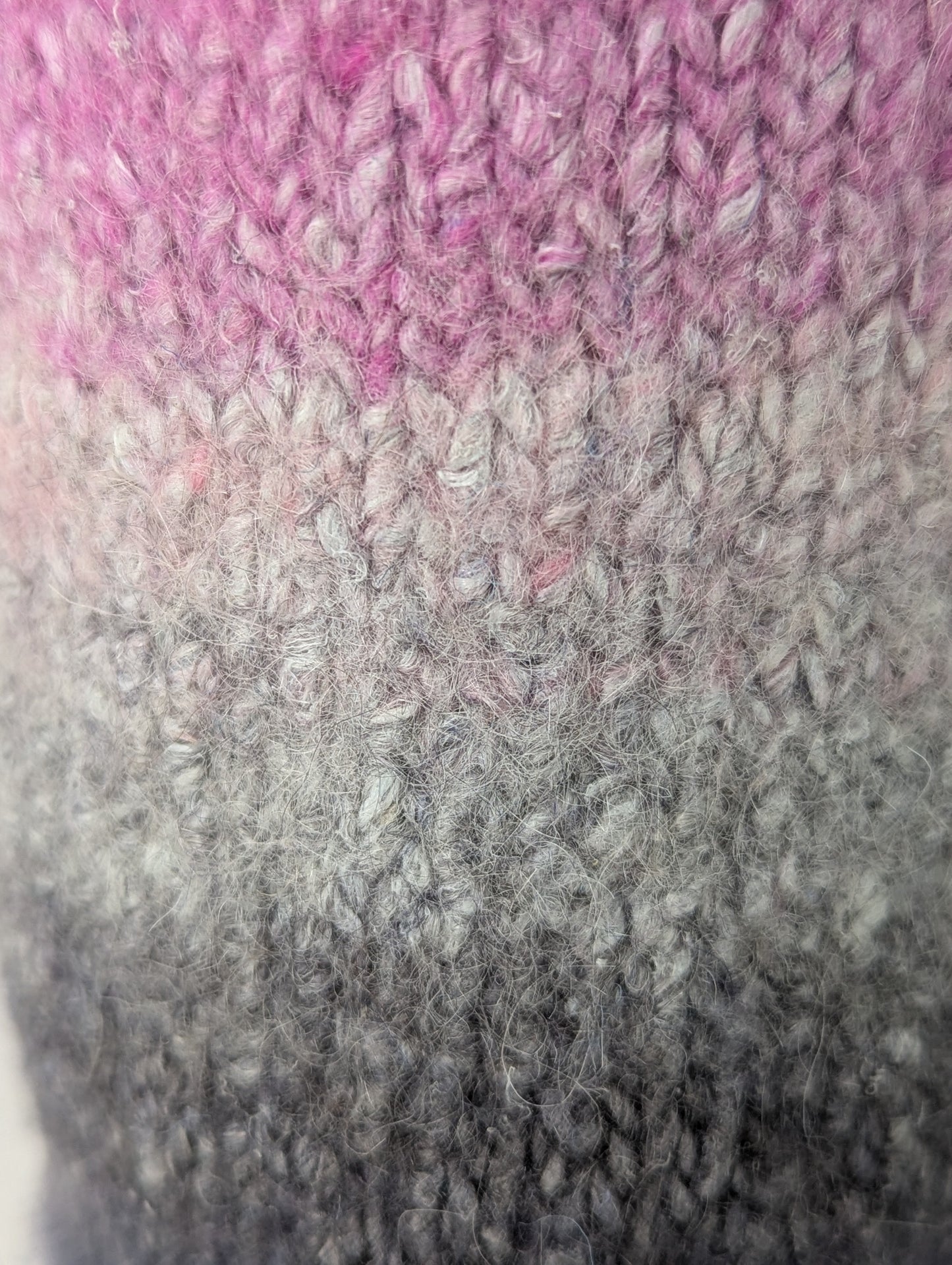 Close-up of a knitted and felted mug cozy in shades of pink, beige, and grey