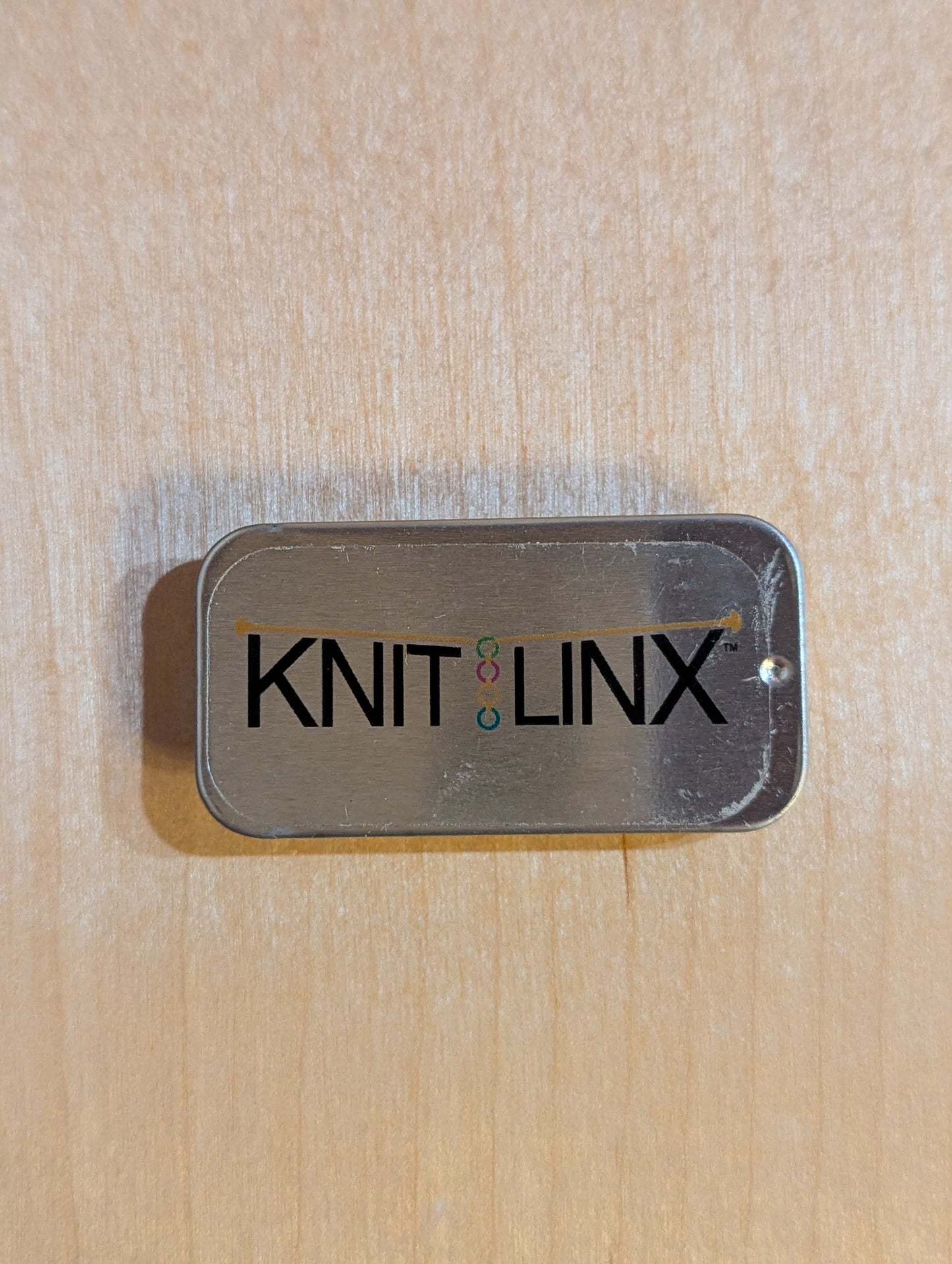 Metal storage box for row counters or stitch markers with 'KNIT LINX' logo on the top.