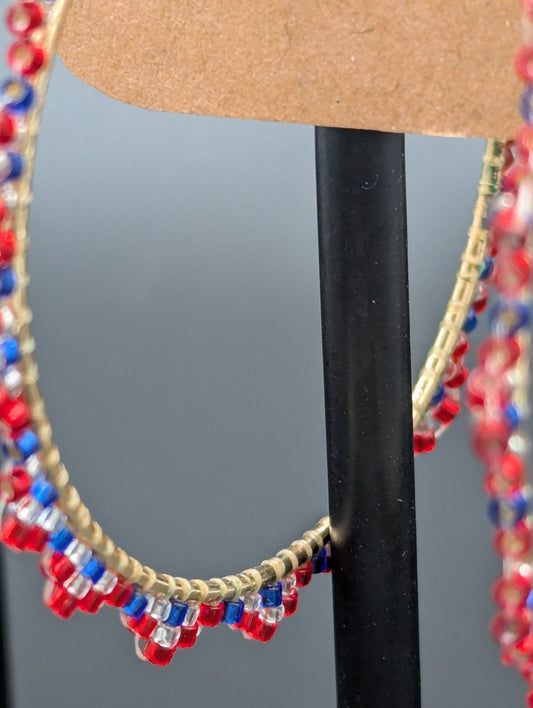 Close up of hand crafted hoop earrings with red, clear and blue glass seed beads sewn onto hoops.