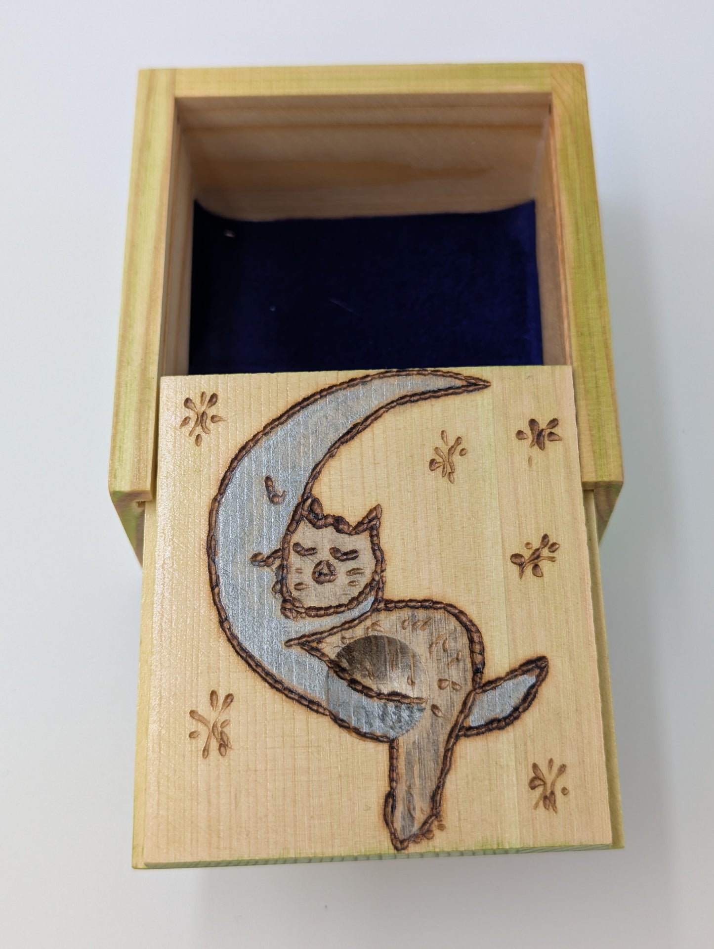 Inside detail of a wood-burned and hand painted trinket box featuring a blue crescent moon and gray cat, lined with blue velvet.