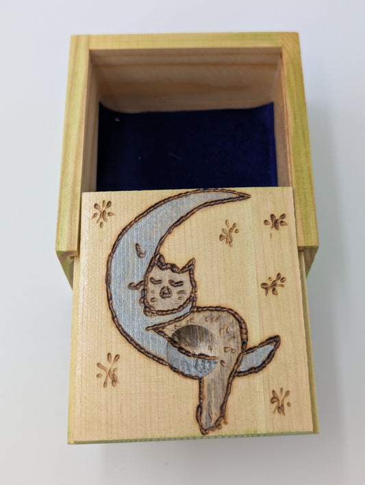Inside detail of a wood-burned and hand painted trinket box featuring a blue crescent moon and gray cat, lined with blue velvet.