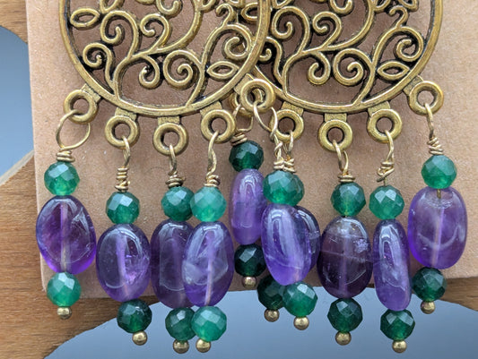 Close up of earrings with gold floral patterns set off by amethyst gemstones and green Swarovski crystal beads.