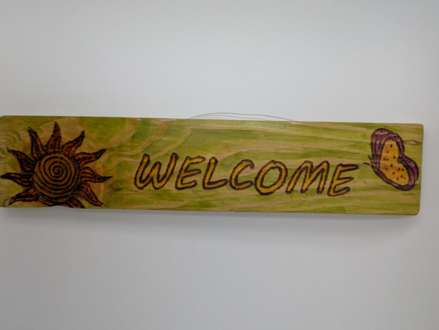 Original wood-burned and hand painted wooden sign with 'WELCOME' text, sun, and butterfly design. Wire hanger to attach to a wall or post.