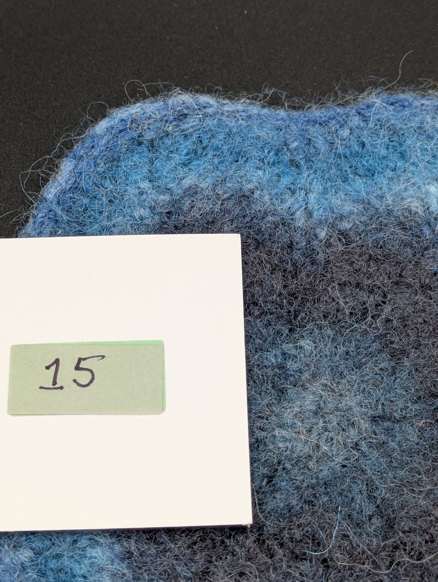 Close up of a blue hand knitted and felted coaster. This coaster is number 15.