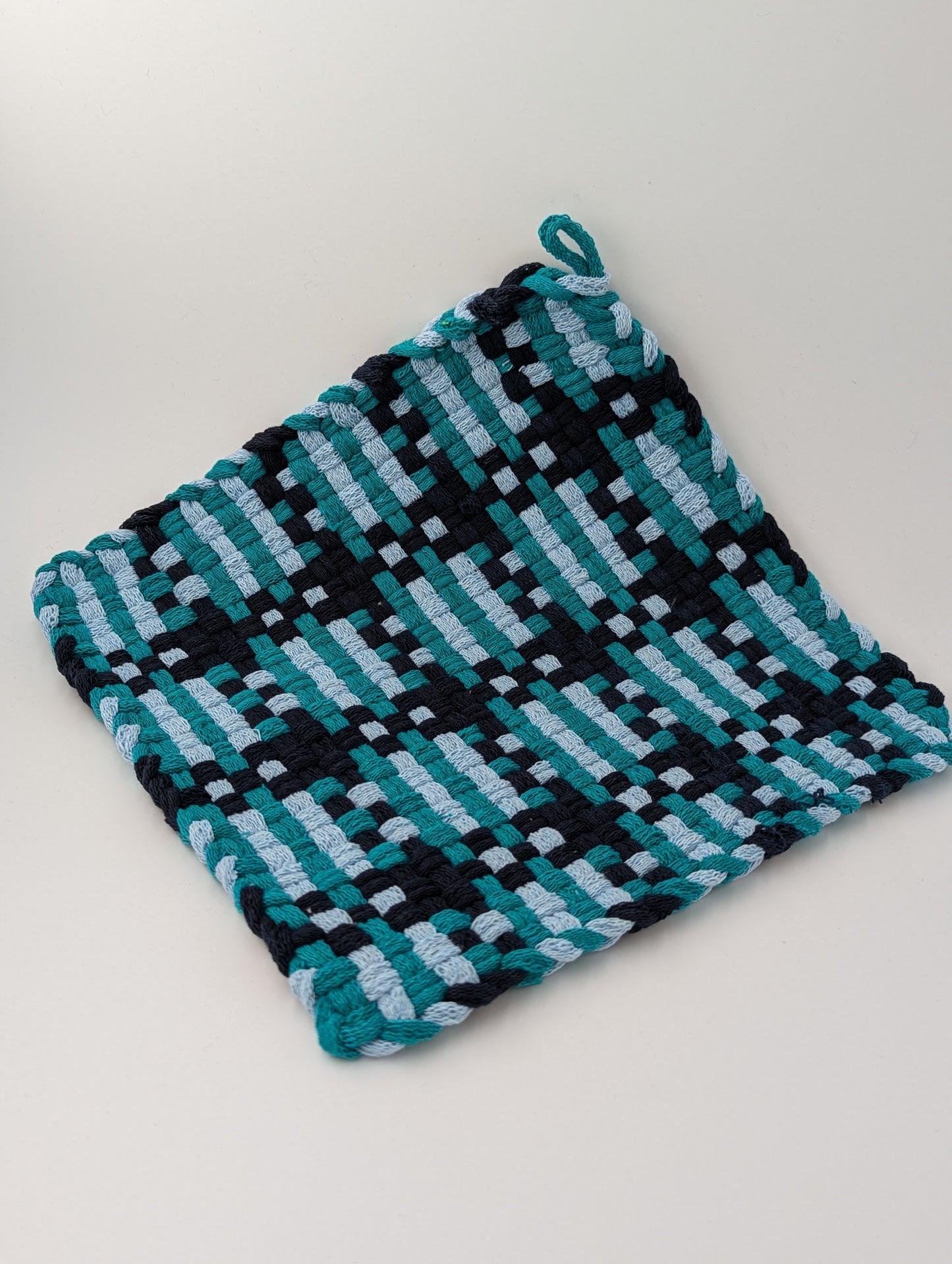 Hand woven trivet in shades of teal, navy, and gray
