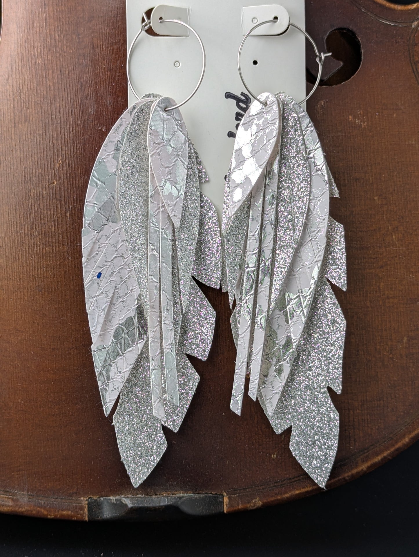 Vegan leather feather-shaped earrings. Sparkly silver and white with silver hoops, 5 inches in length