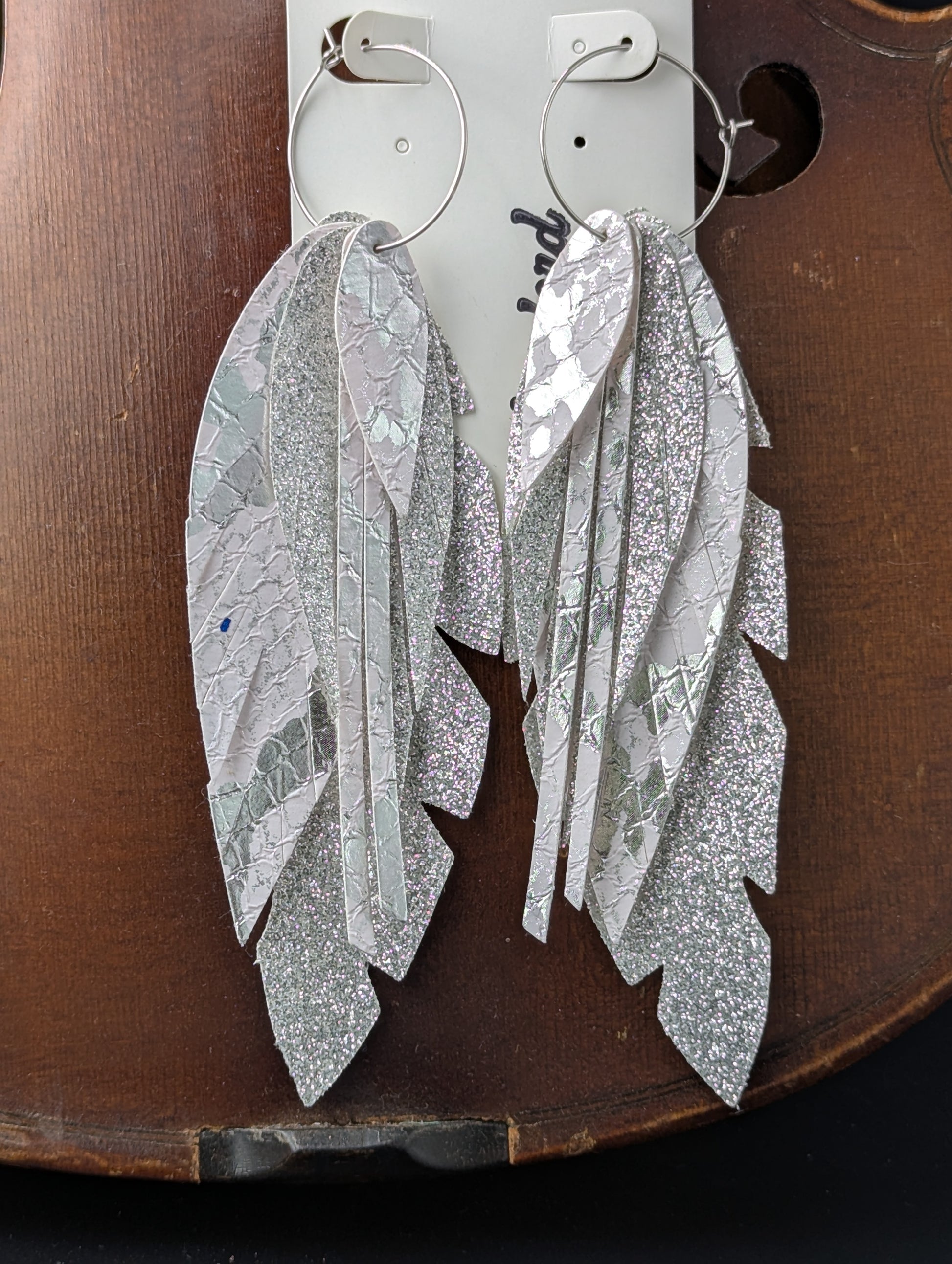 Vegan leather feather-shaped earrings. Sparkly silver and white with silver hoops, 5 inches in length