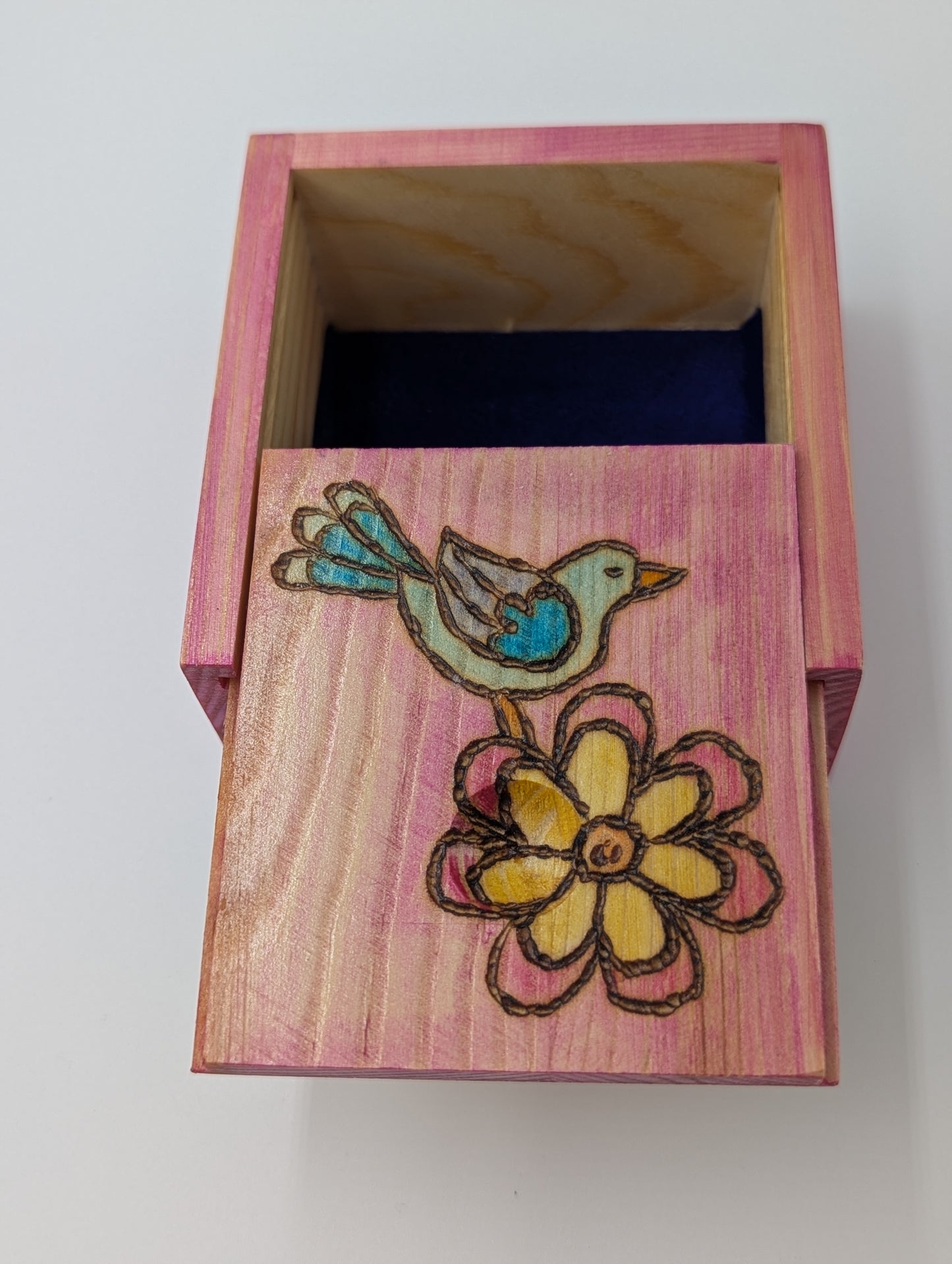 Inside detail of wood-burned, hand painted wooden trinket box with a bluebird and flower on a pink background. Interior lining is blue velvet.