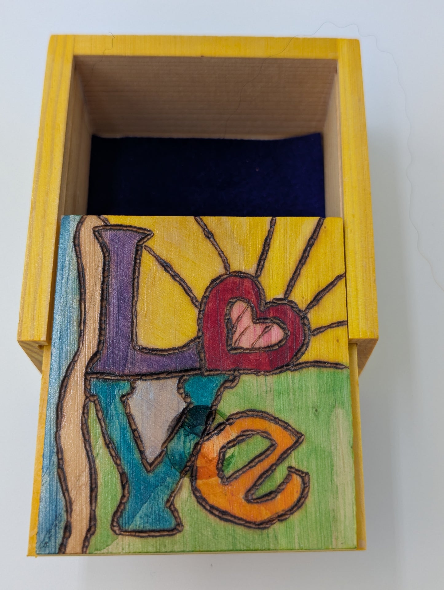 Inside of wood-burned and hand painted trinket box in vibrant colors with the word 'Love'.