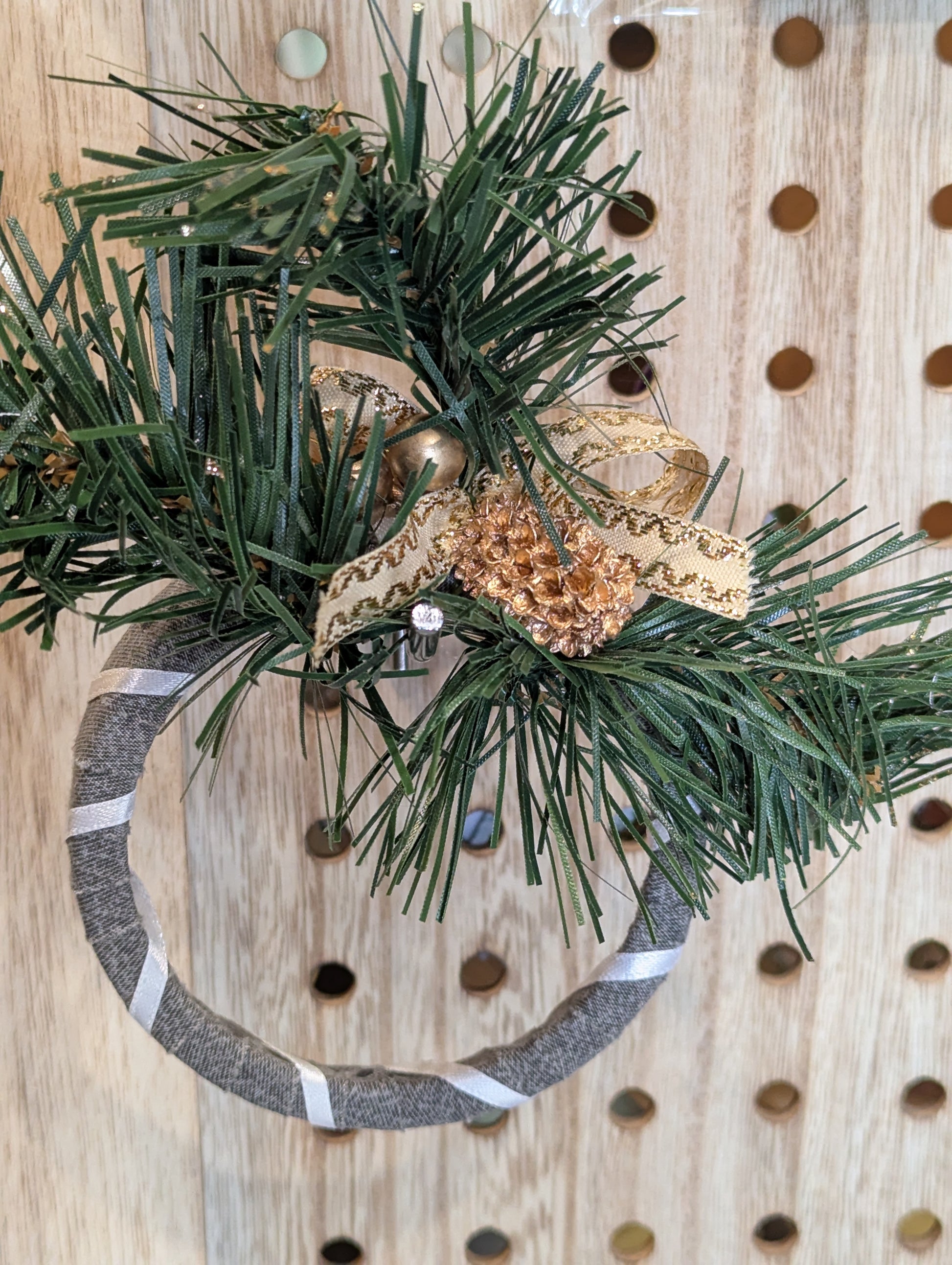 Decorative wreath with white ribbon and fold ornaments nestled in faux pine branches. 