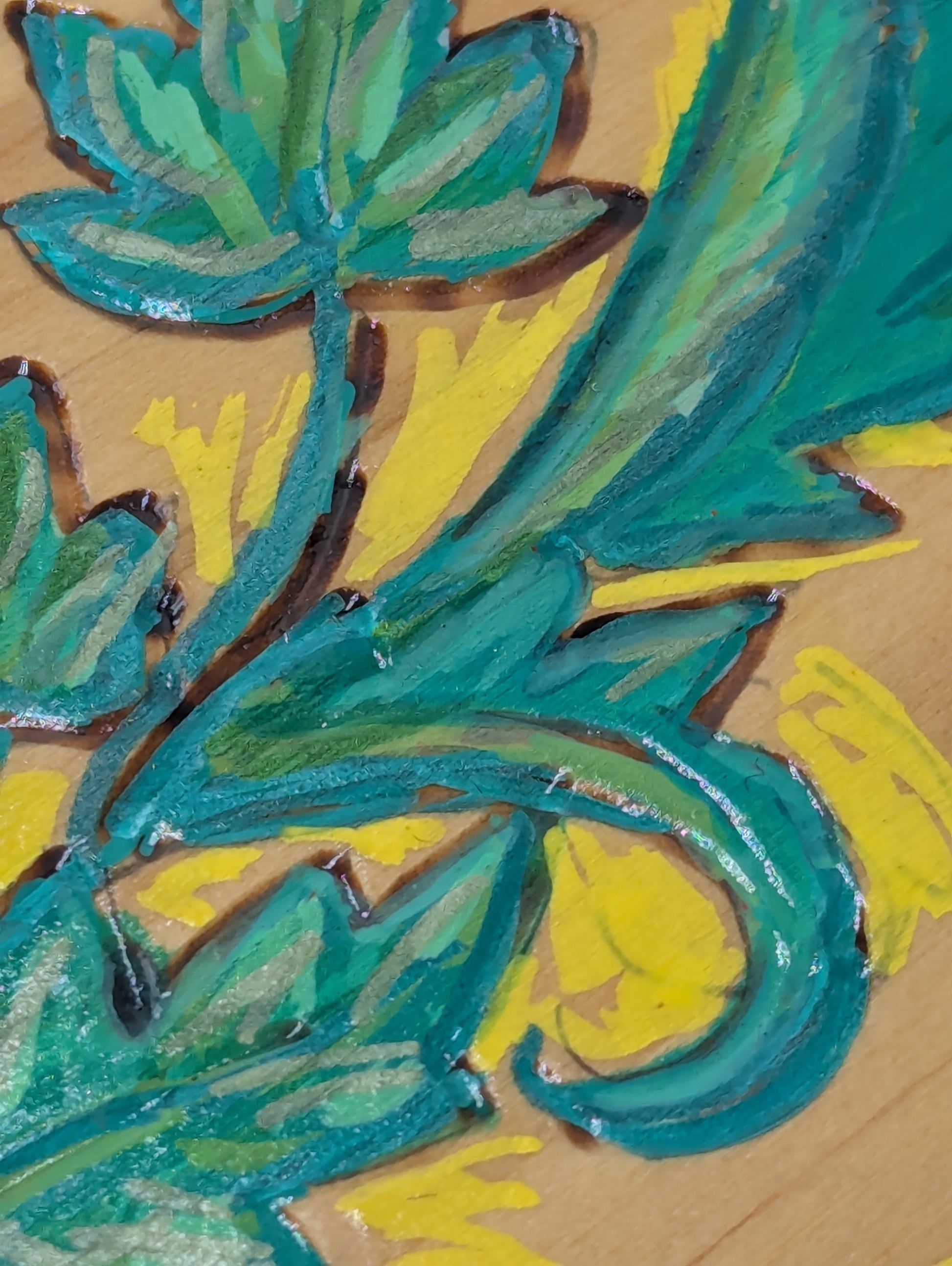 Close up of a wooden coaster, wood burned and tole painted with a green leaf design 