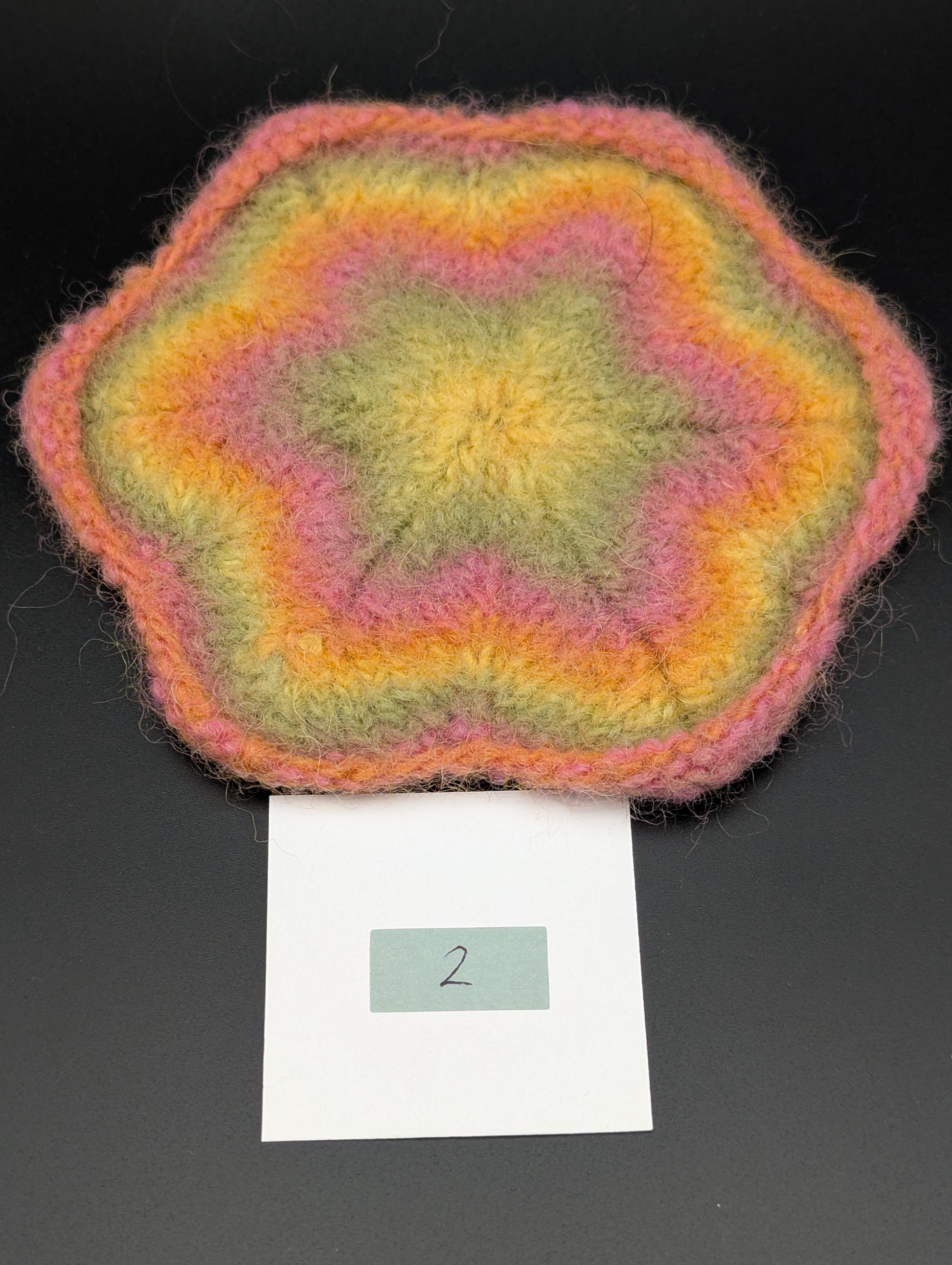 Multicolored knitted and felted coaster in shades of pink, green and yellow. This coaster is style number 2. 