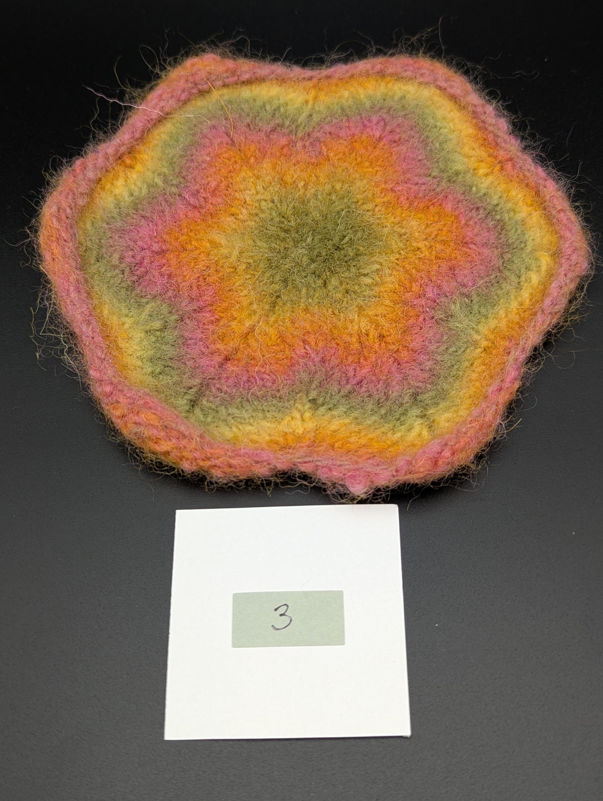 Multicolored knitted and felted coaster in shades of pink, green and yellow. This coaster is style number 3. 