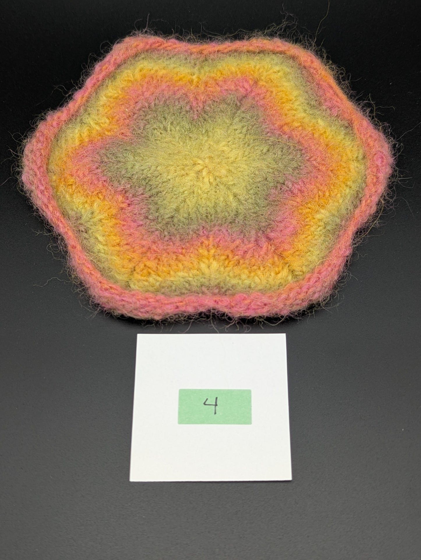 Multicolored knitted and felted coaster in shades of pink, green and yellow. This coaster is style number 4. 