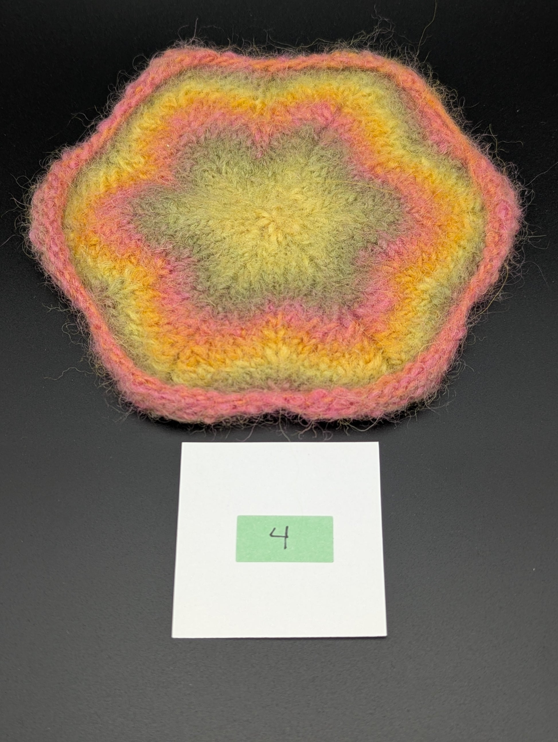 Multicolored knitted and felted coaster in shades of pink, green and yellow. This coaster is style number 4. 