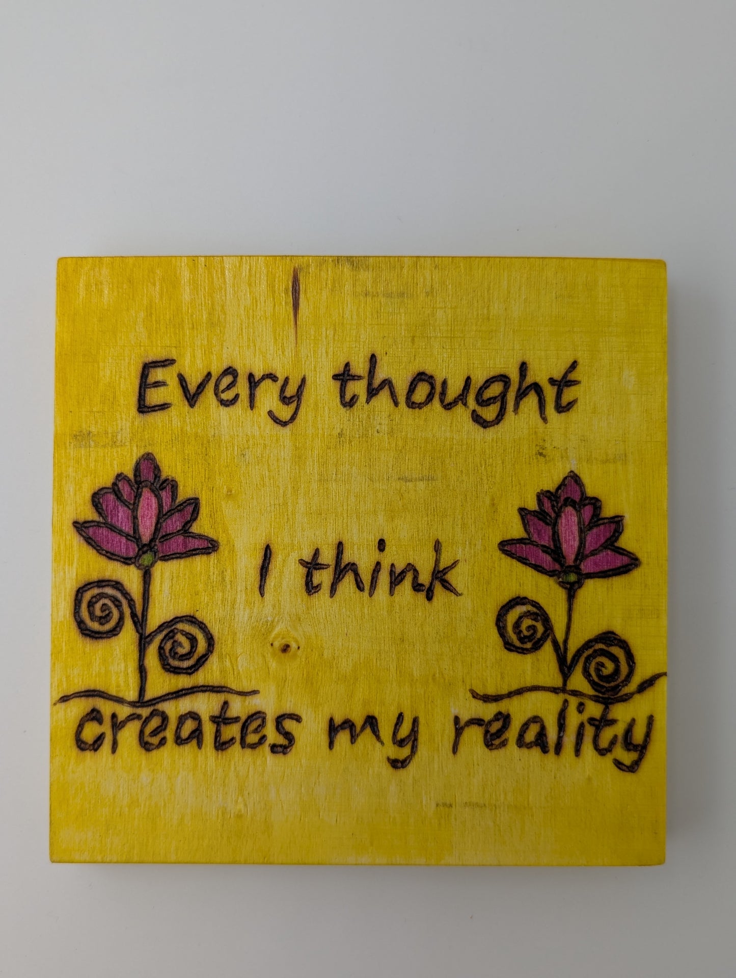 Original wood-burned and hand painted wall art. 'Every thought I think creates my reality'. Yellow background with pink flowers.