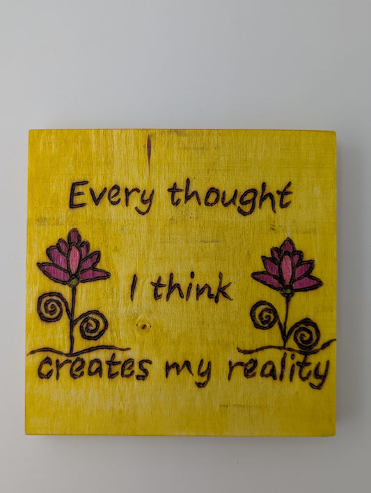 Original wood-burned and hand painted wall art. 'Every thought I think creates my reality'. Yellow background with pink flowers.