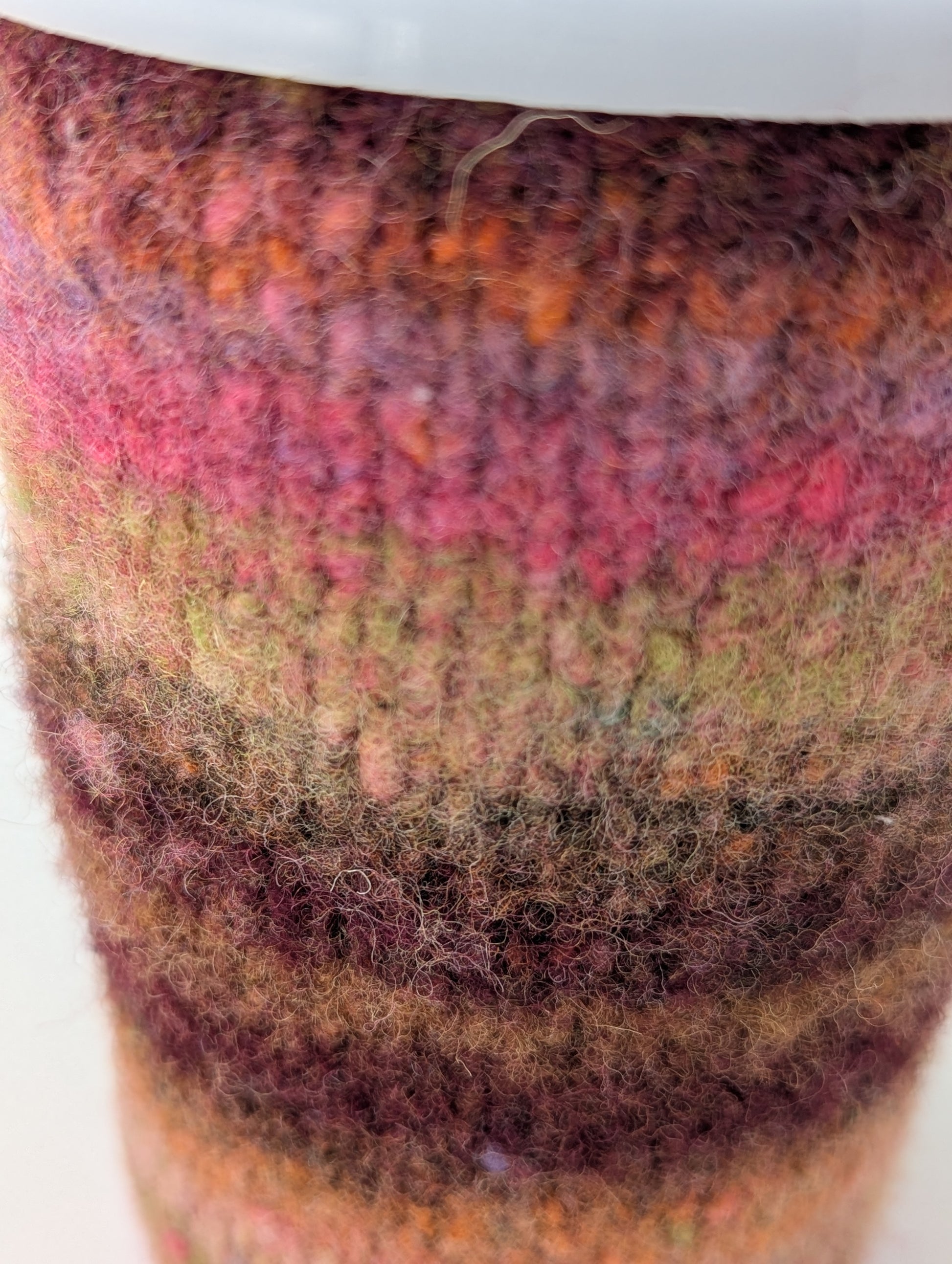 Close-up of a striped knitted and felted mug cozy in shades of pink and brown