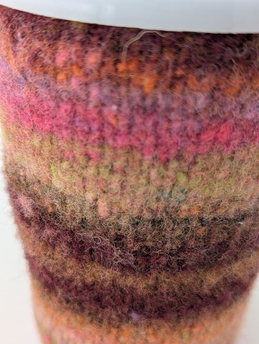 Close-up of a striped knitted and felted mug cozy in shades of pink and brown