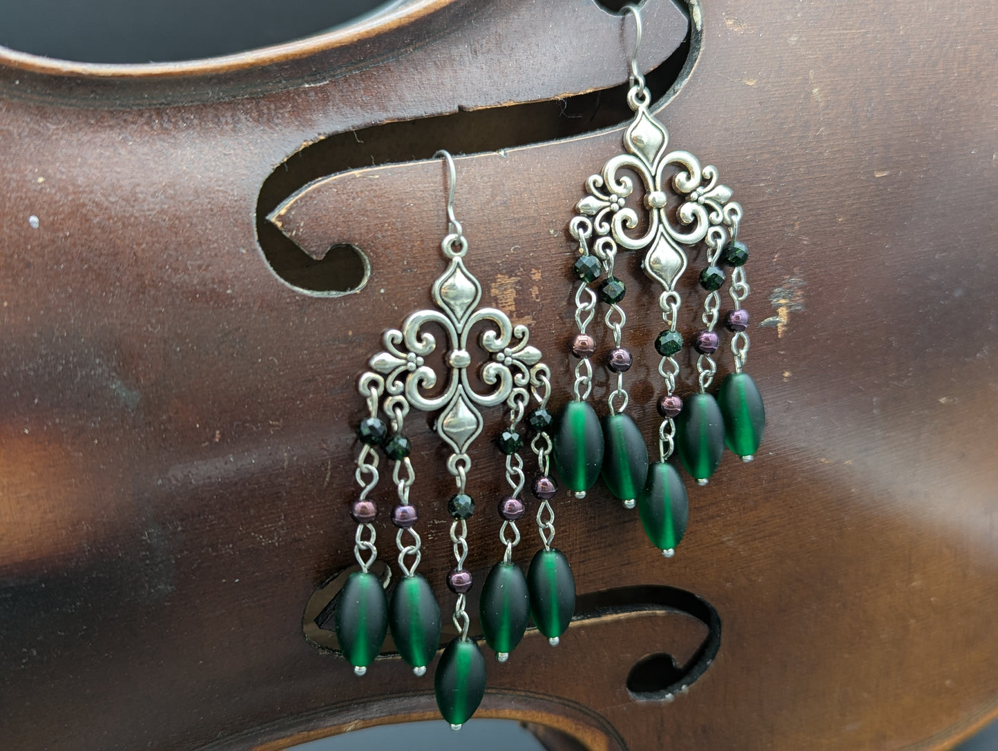 Pair of earrings featuring silver fleur-de-lis with green glass beads highlighted by green crystal beads and Garnet gemstones.