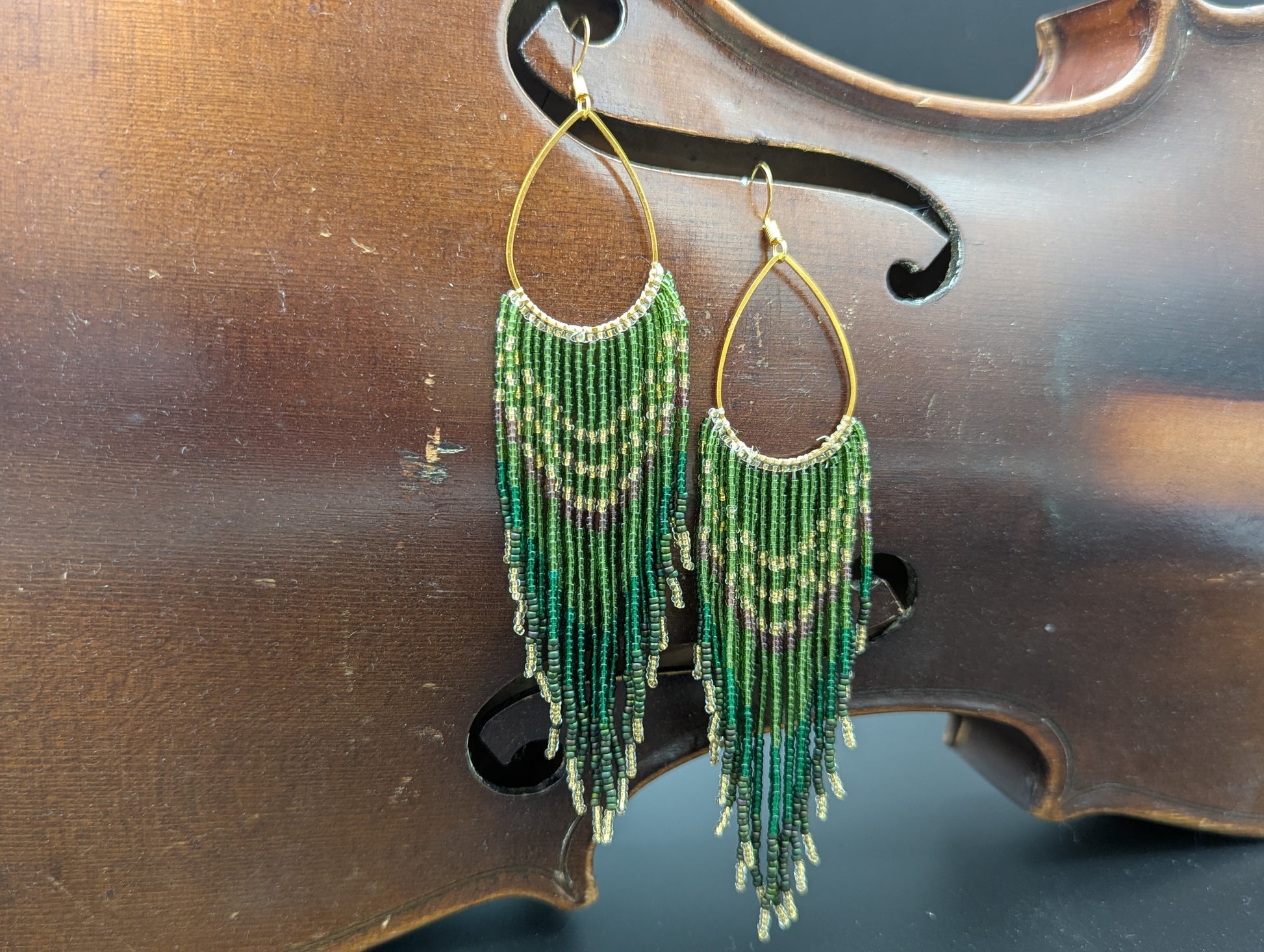 Green, gold, clear, purple, turquoise and silver glass seed beads trail down from a gold teardrop.