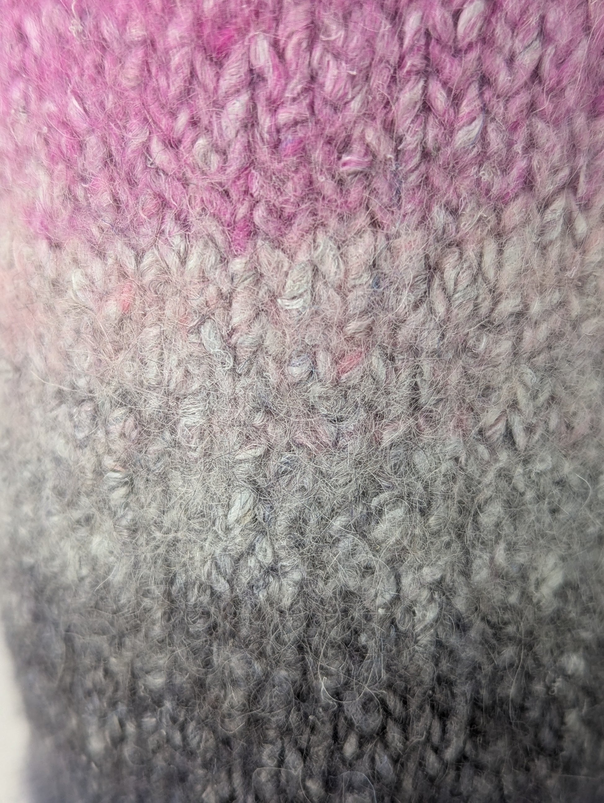 Close-up of a knitted and felted mug cozy in shades of pink, beige, and grey
