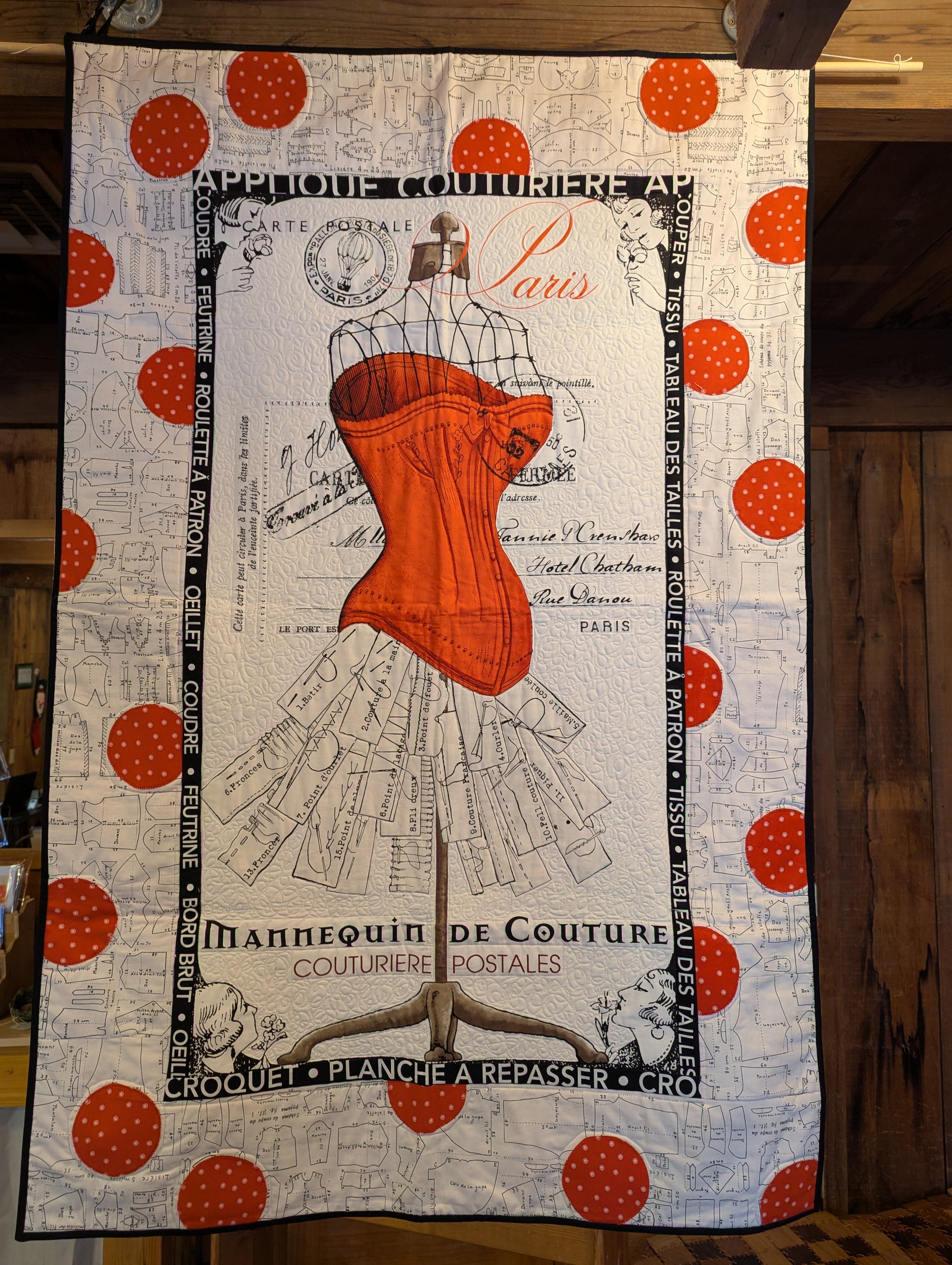Hand made quilt, lap sized, featuring an image of Mannequin de Couture in red and black on a white background. This quilt also includes a hanging pocket on the back so that it can be displayed on a wall, if you choose