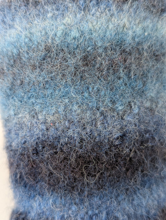 Close-up of a knitted and felted mug cozy in shades of blue and grey