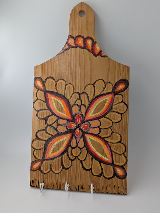 Decorative wooden cutting board with a wood burned and tole painted flower design and 3 cup hooks along the lower edge.