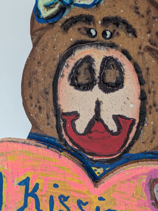 Close up of a wooden bear figurine with a heart-shaped sign saying 'Kissing Booth 50 Cents'