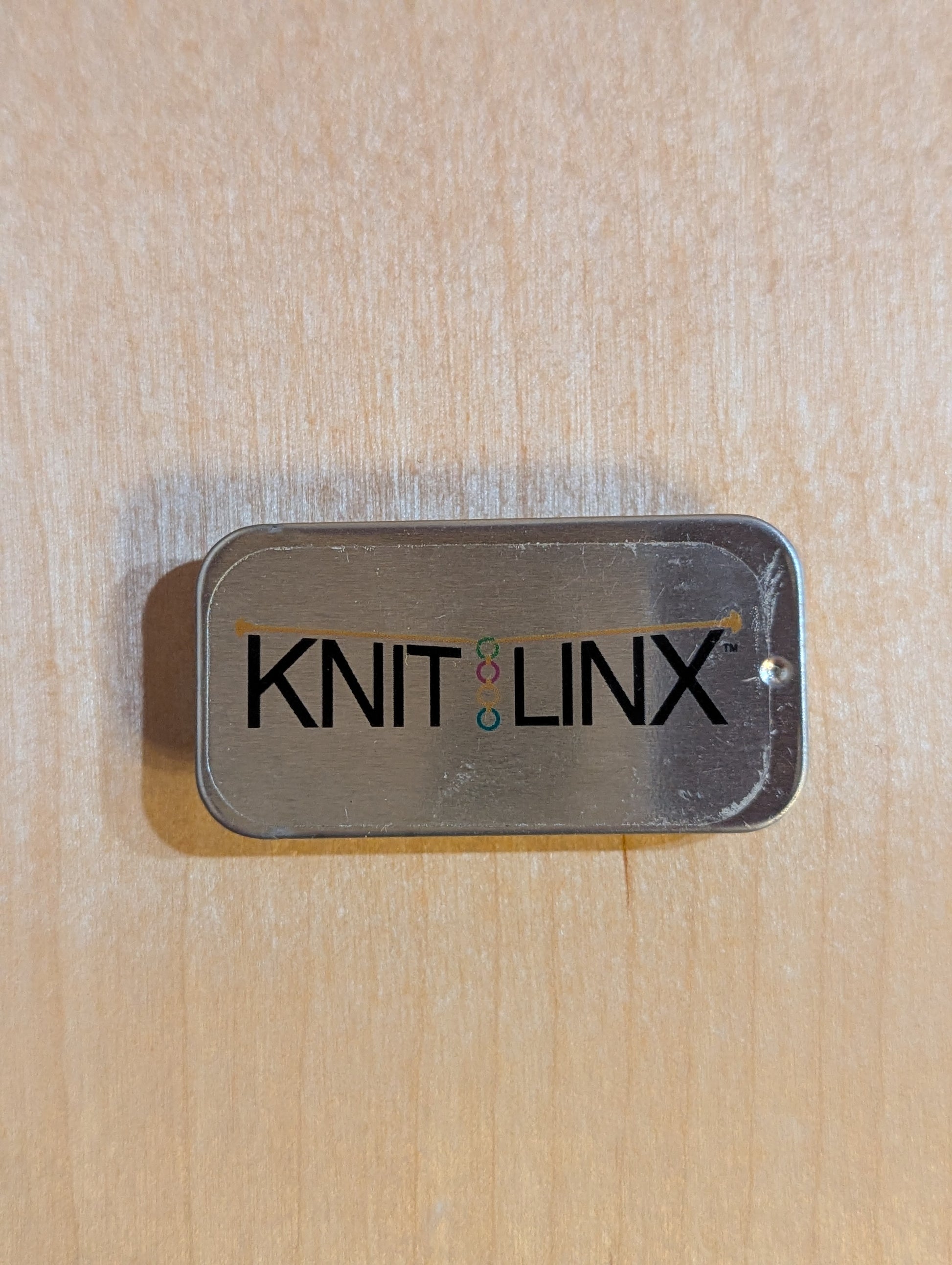 Metal storage box for row counters or stitch markers with 'KNIT LINX' logo on the top.