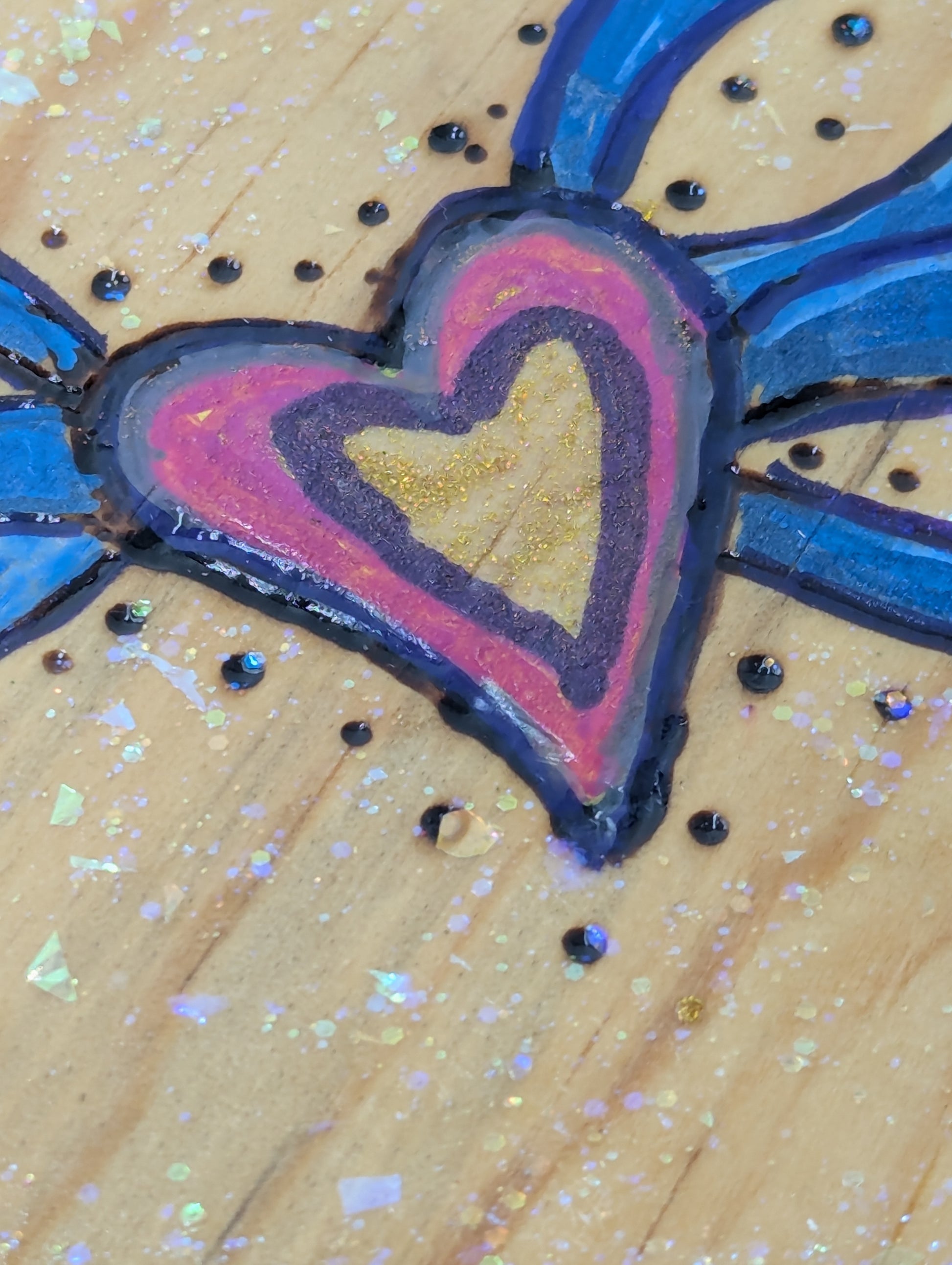 Close up of a decorative wooden heart-shaped plaque with blue and pink designs.