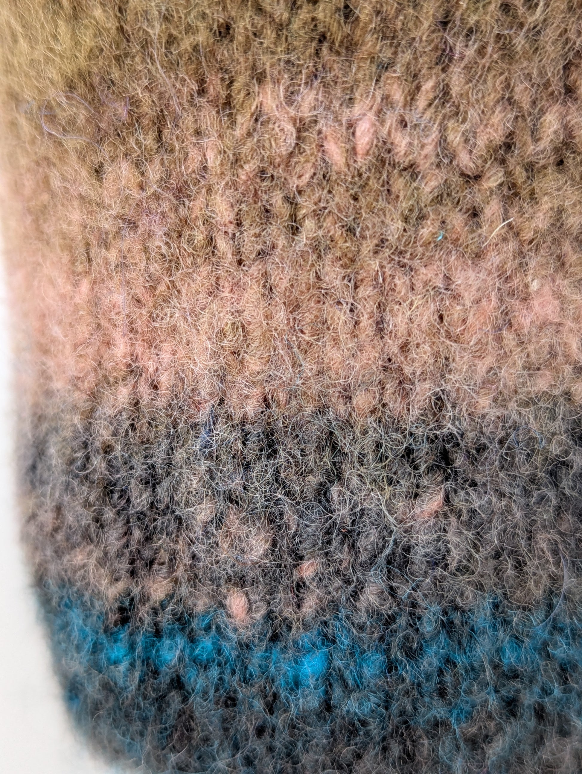 Close-up of a knitted and felted mug cozy with a brown to blue color gradient