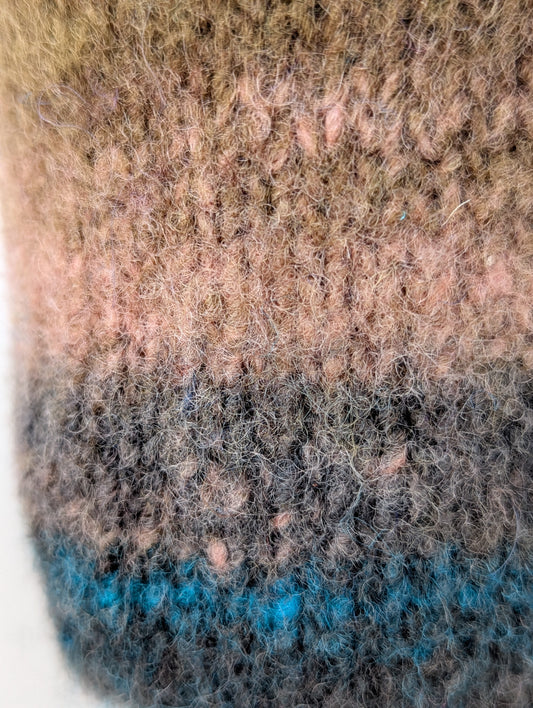 Close-up of a knitted and felted mug cozy with a brown to blue color gradient