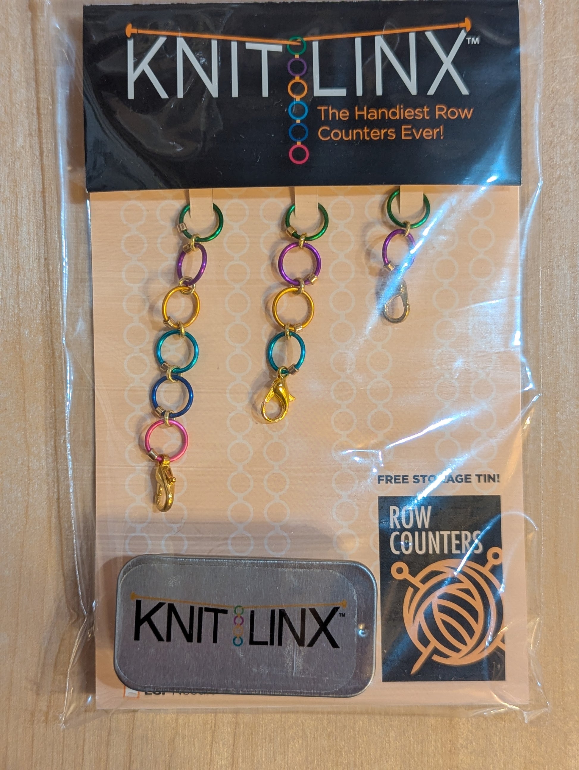 Knitting row counters by KnitLinx in 3 different chain lengths that can be used together, along with a metal storage tin. For knitting needles size 0 through 8. Made of metal in assorted colors.