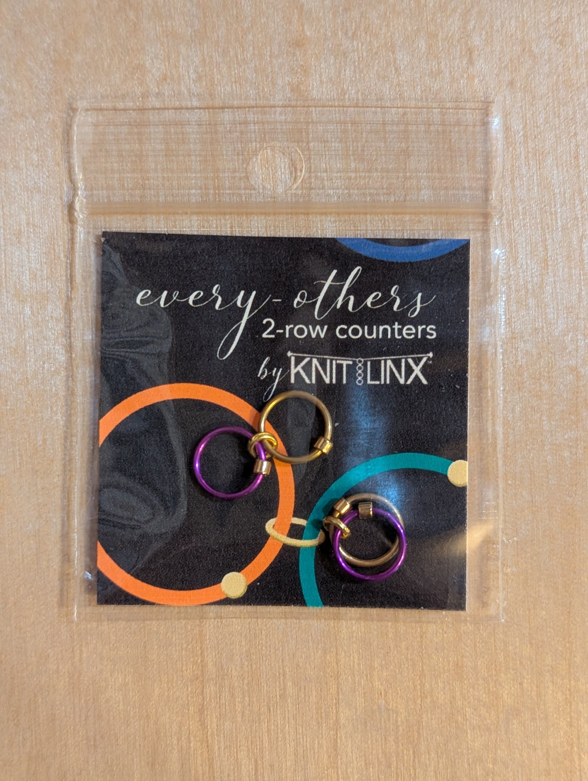 Packaged set of 'every-others' 2-row counters by Knit Linx for knitting needles size 0 through 8 in gold and purple colors.
