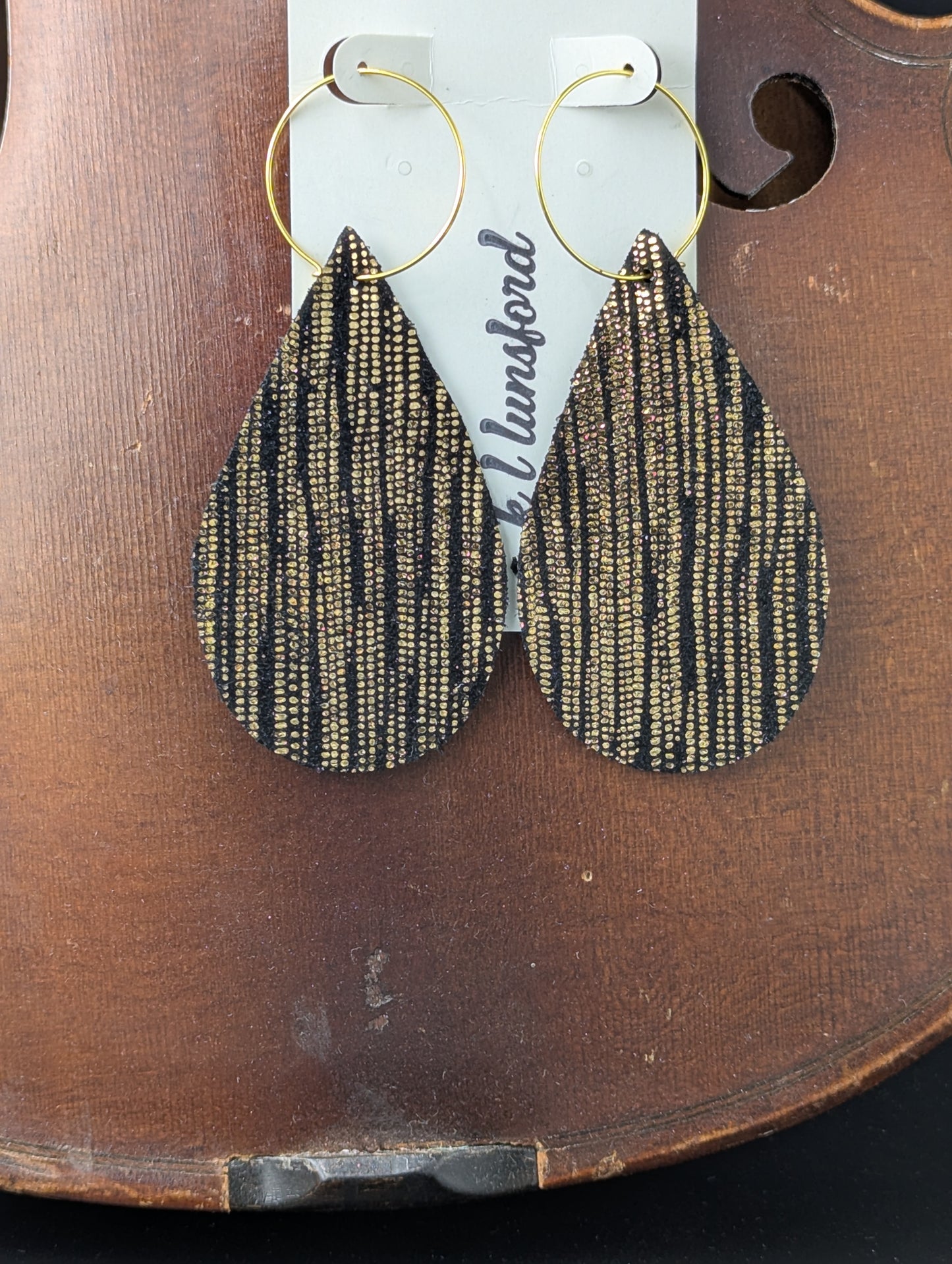 Teardrop shaped black leather earrings with gold accents on gold hoops. 3.5 inches long