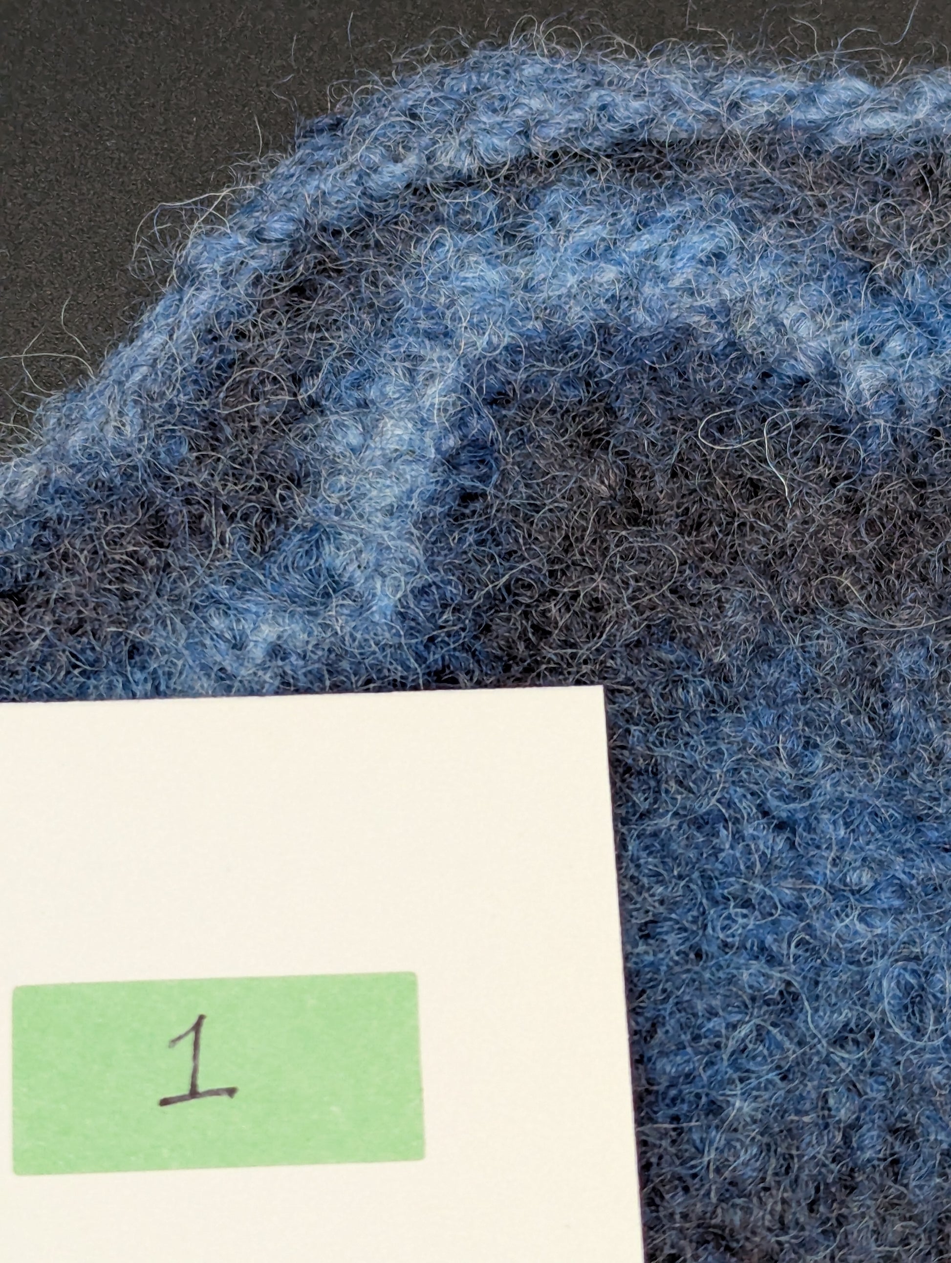 Close up of a blue hand knitted and felted coaster. This coaster is number 1.