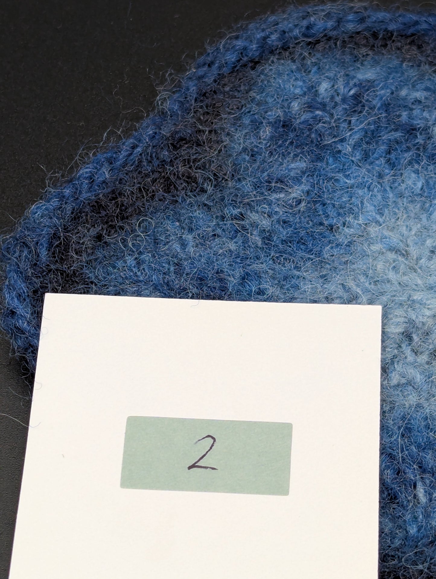 Close up of a blue hand knitted and felted coaster. This coaster is number 2.