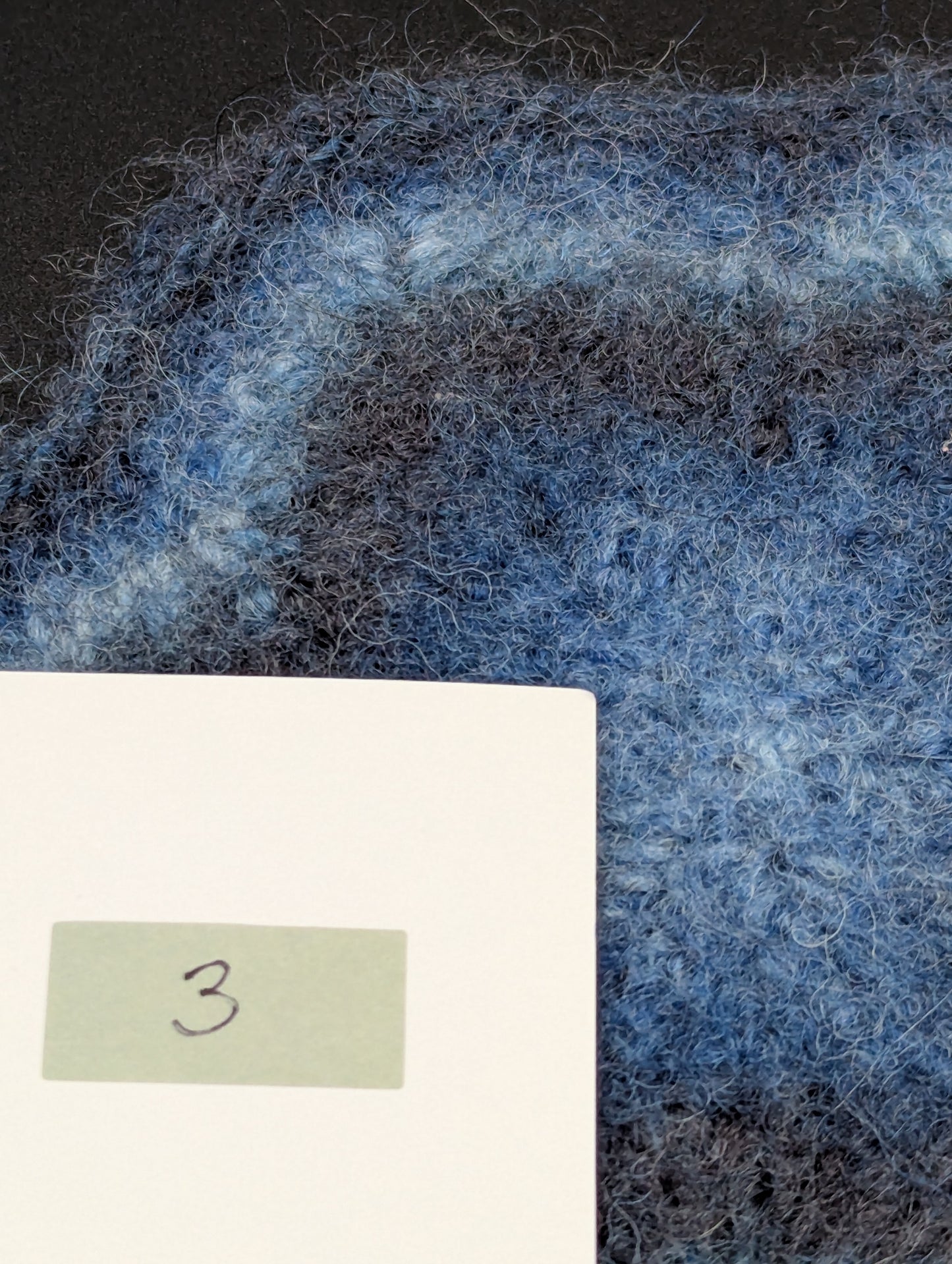 Close up of a blue hand knitted and felted coaster. This coaster is number 3.