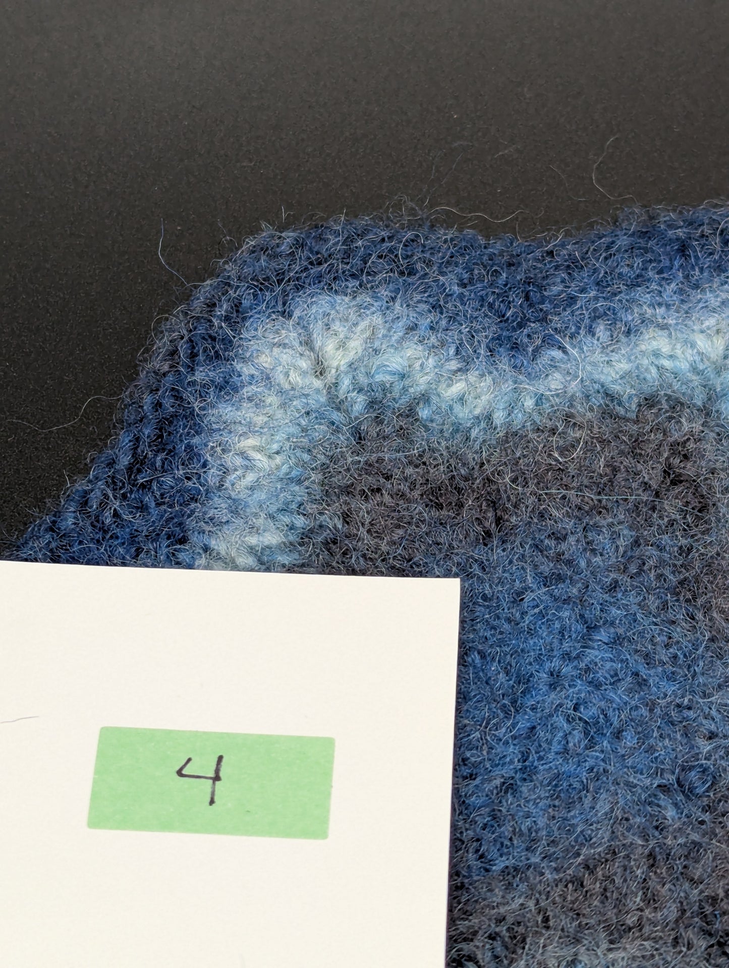Close up of a blue hand knitted and felted coaster. This coaster is number 4.