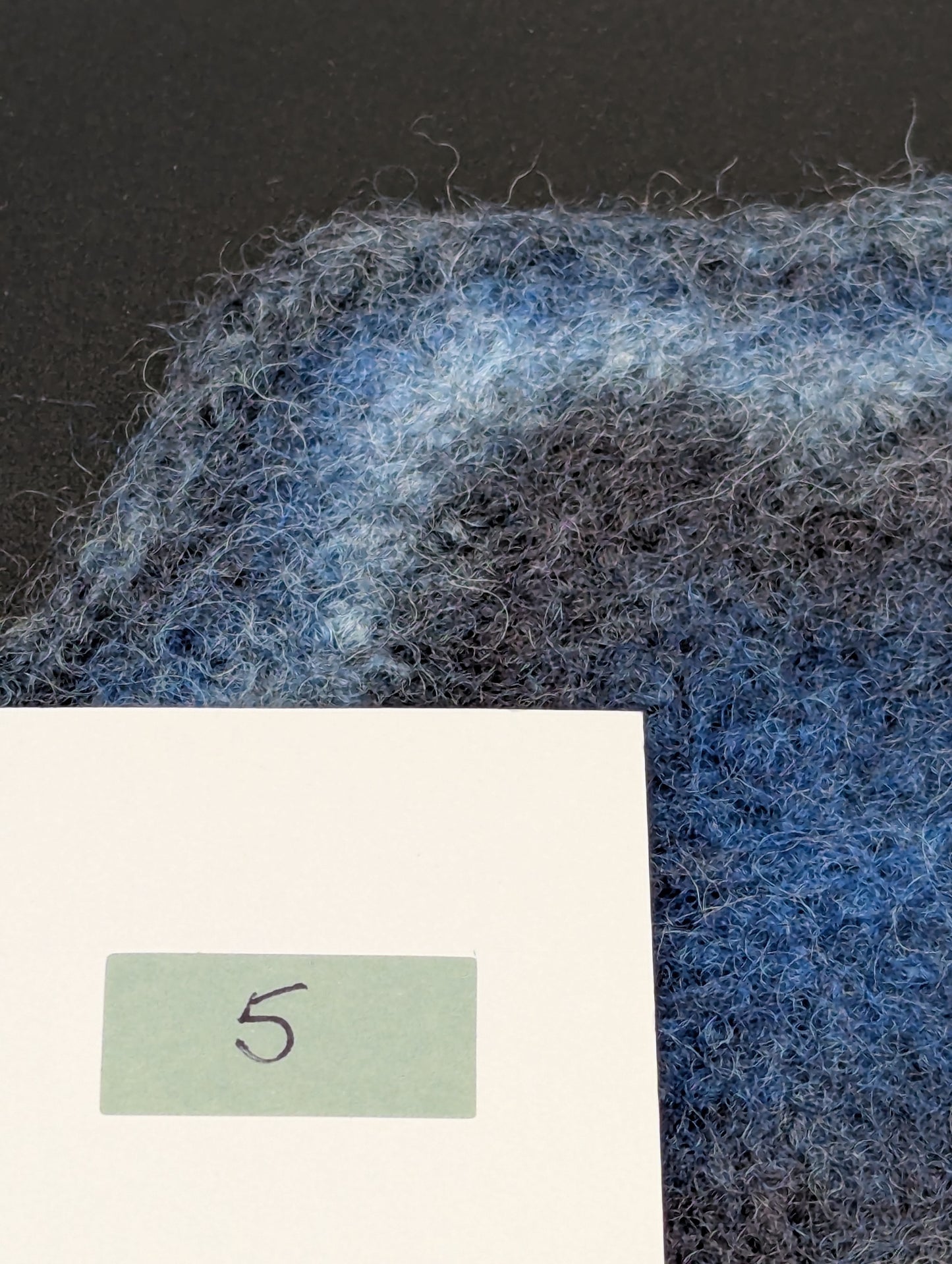 Close up of a blue hand knitted and felted coaster. This coaster is number 5.