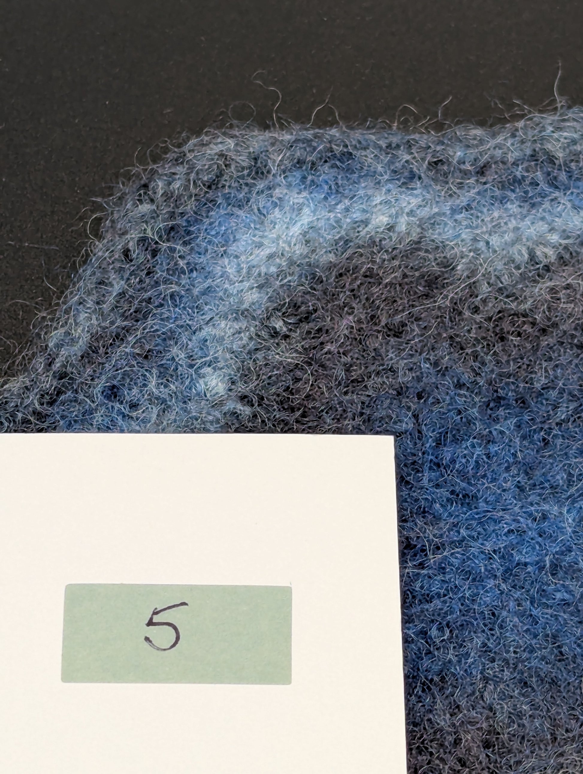 Close up of a blue hand knitted and felted coaster. This coaster is number 5.