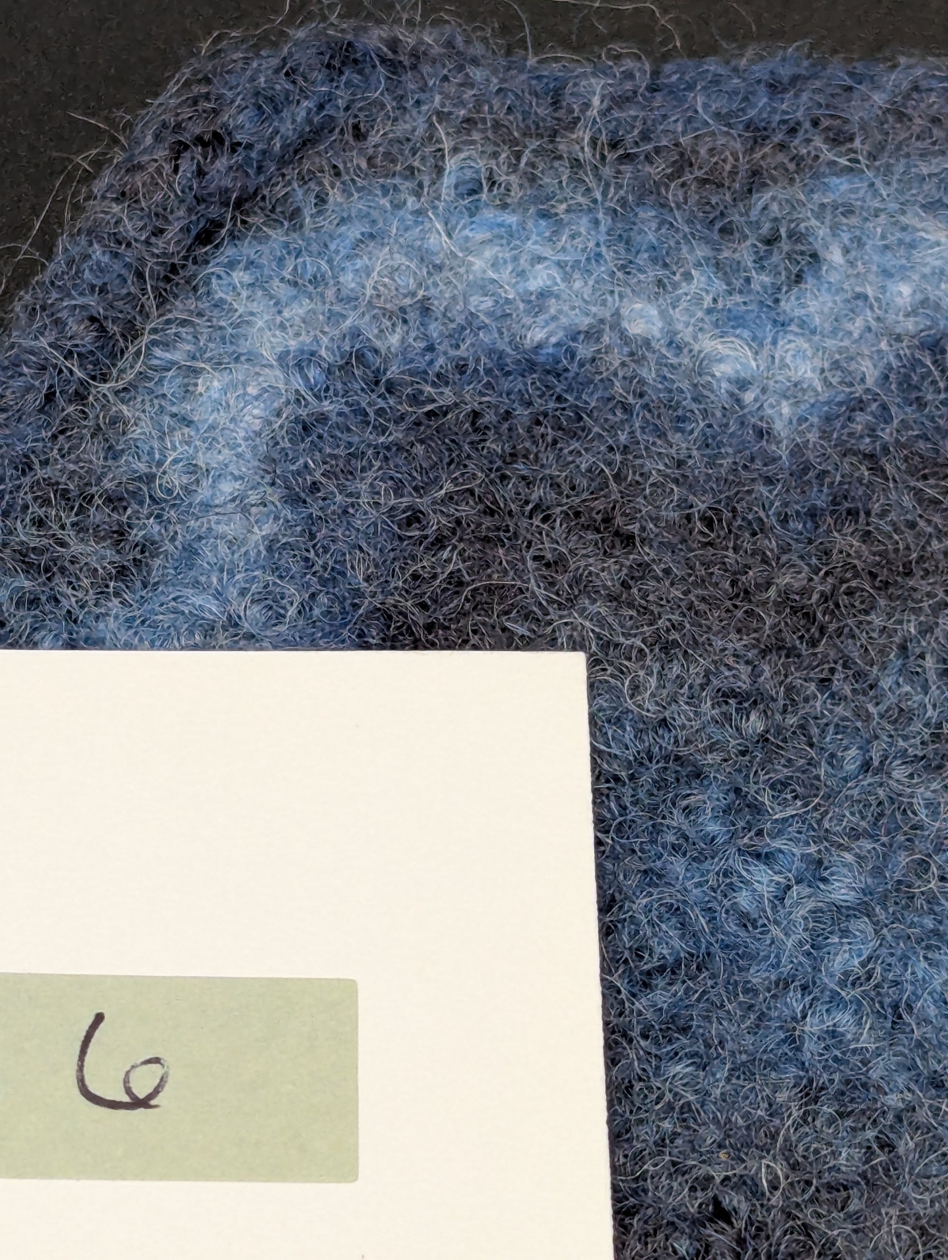 Close up of a blue hand knitted and felted coaster. This coaster is number 6.