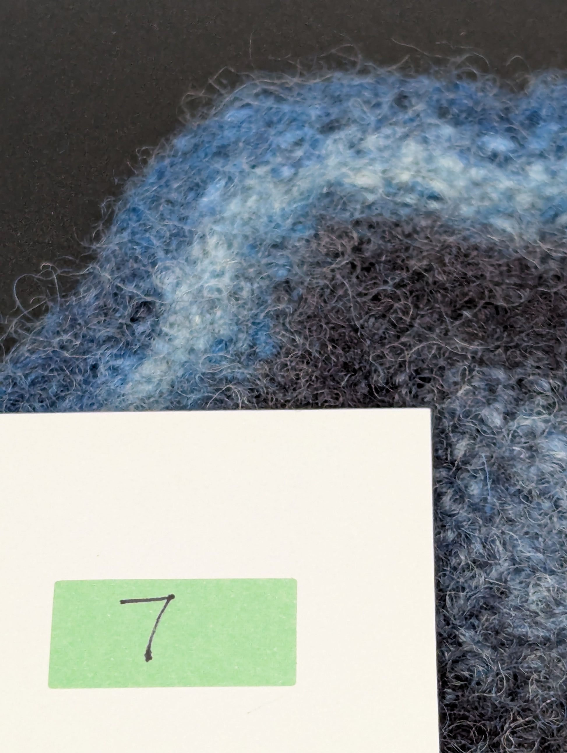 Close up of a blue hand knitted and felted coaster. This coaster is number 7.