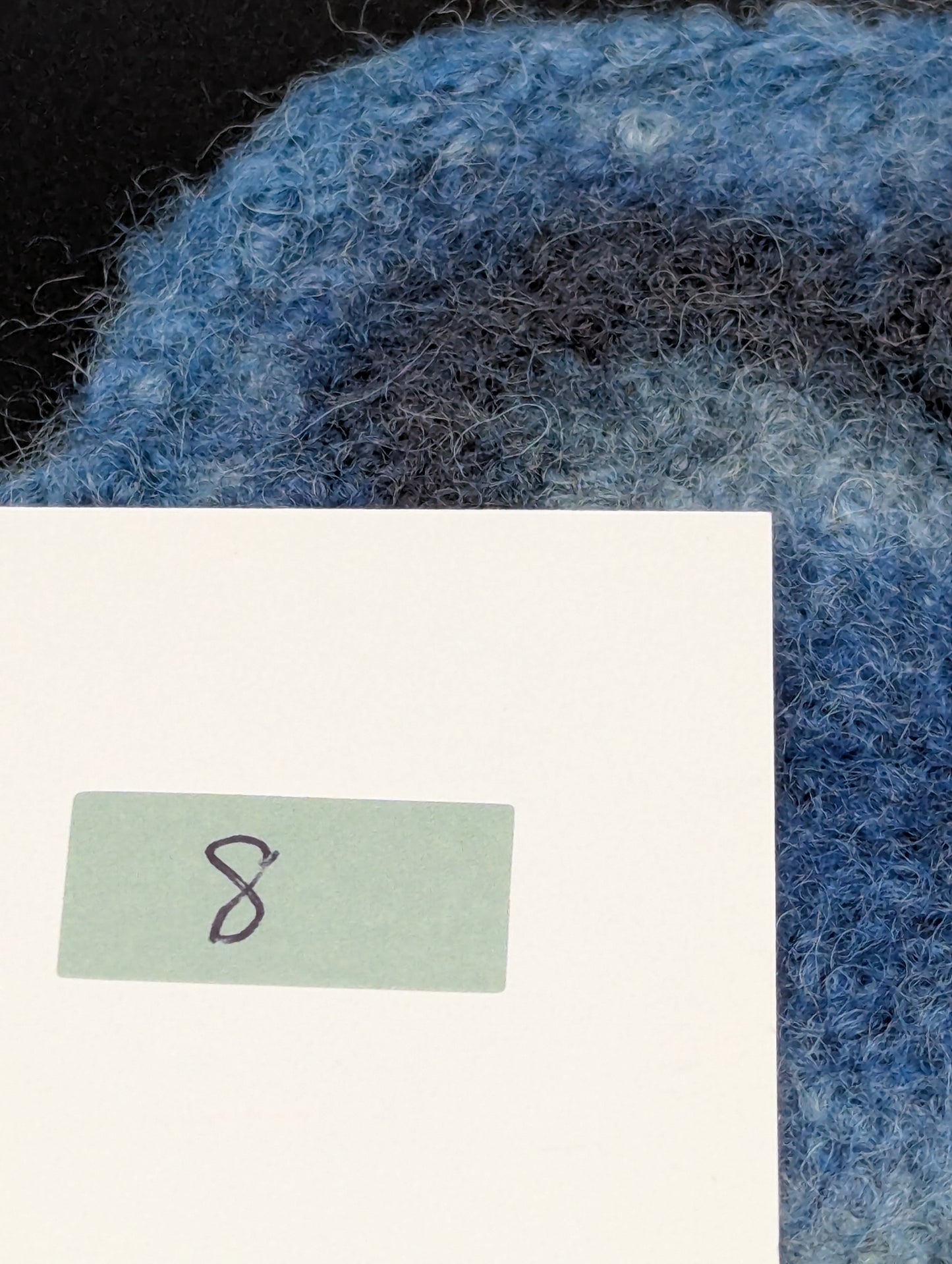 Close up of a blue hand knitted and felted coaster. This coaster is number 8.