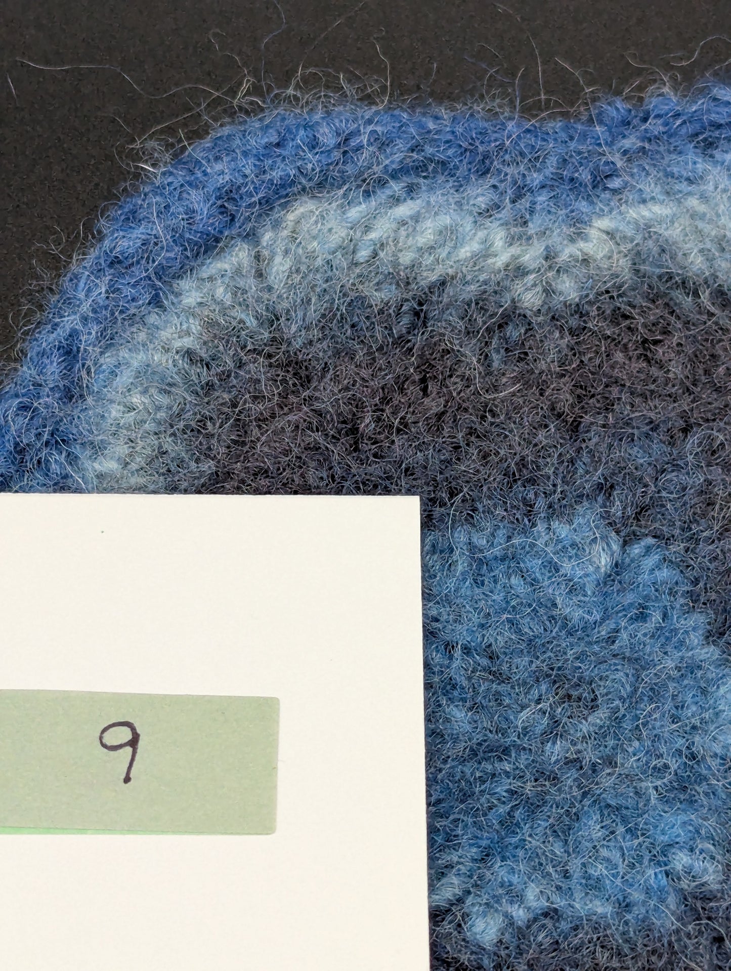 Close up of a blue hand knitted and felted coaster. This coaster is number 9.
