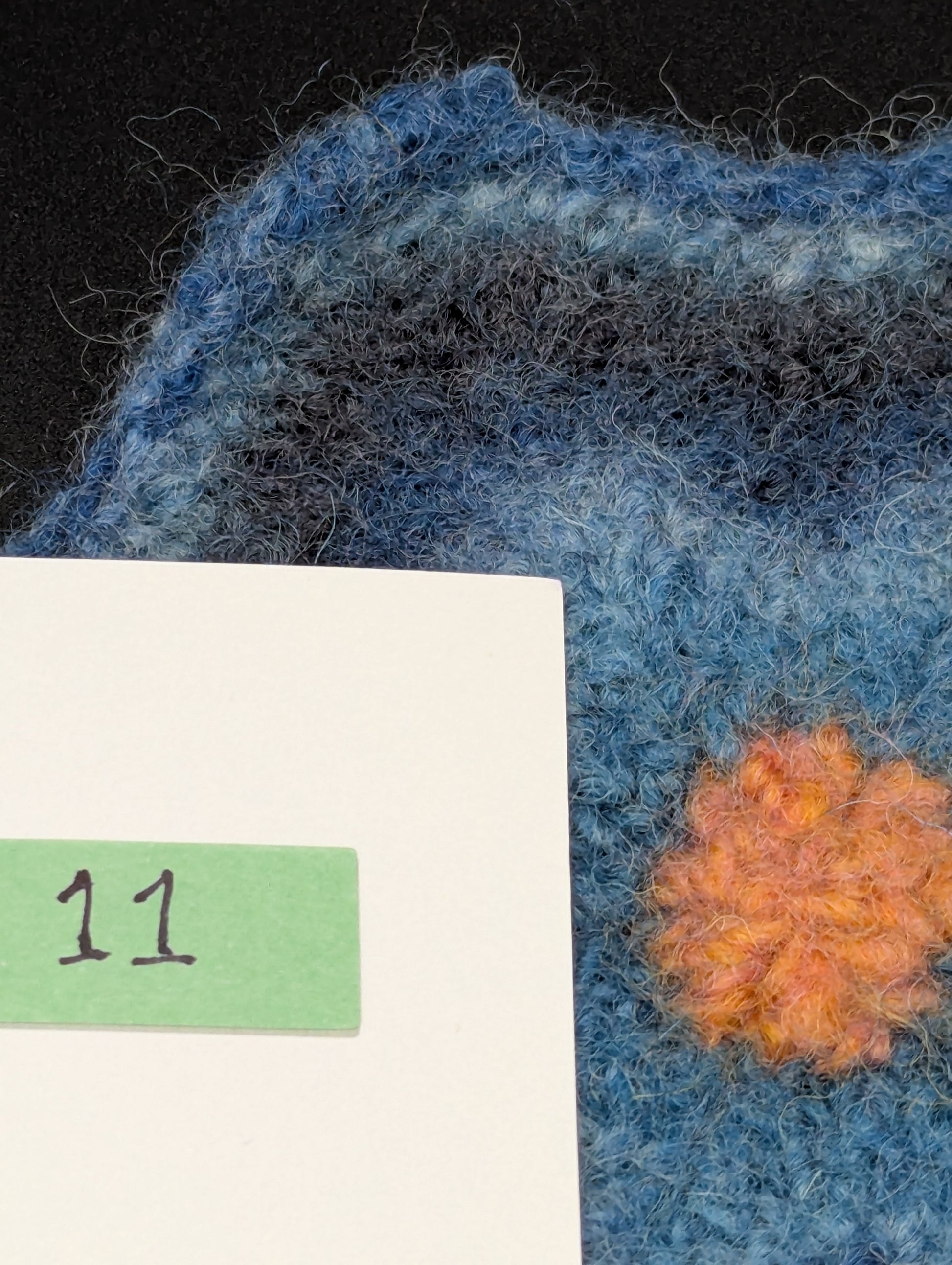 Close up of a blue hand knitted and felted coaster. This coaster is number 11.