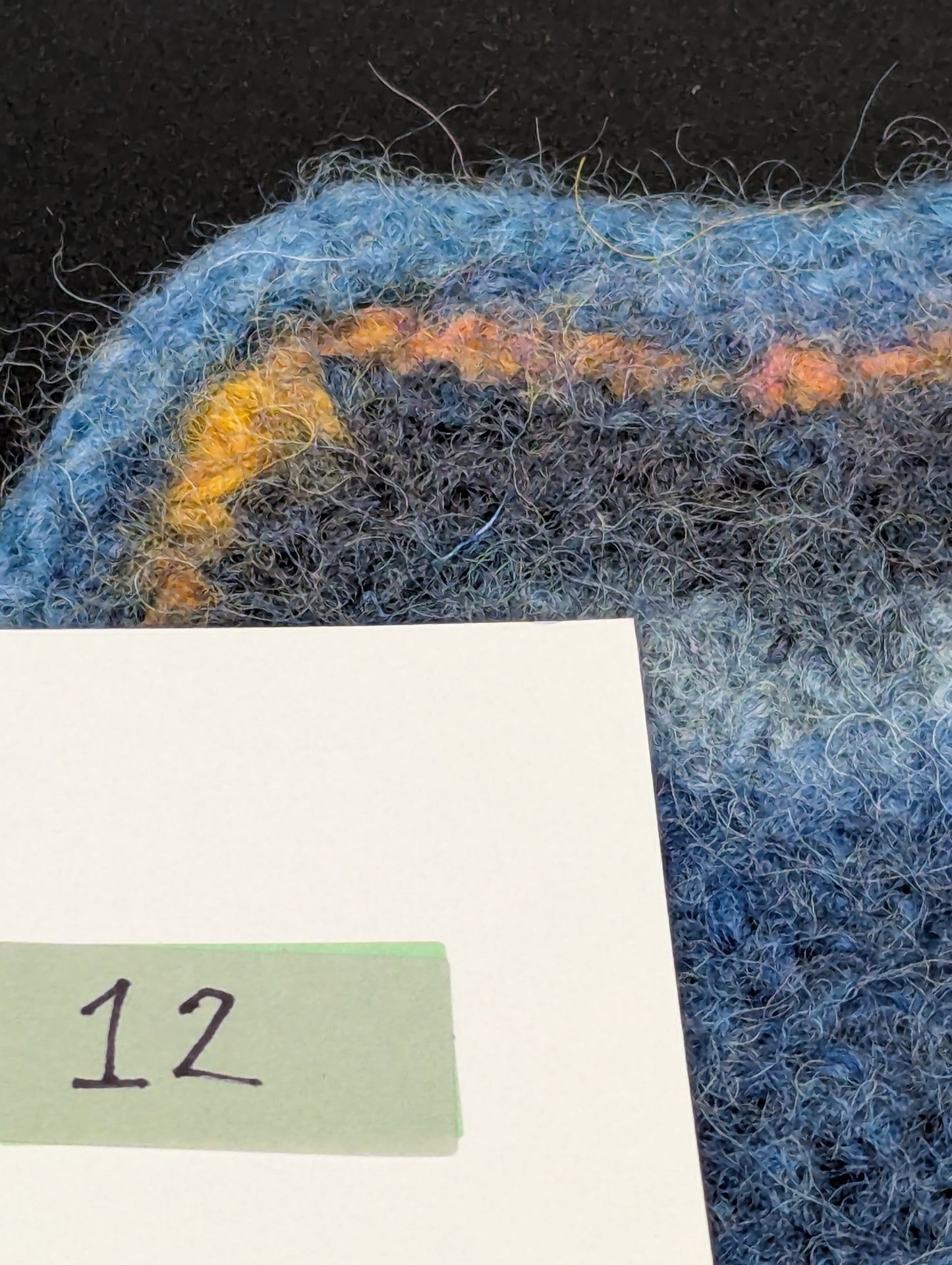 Close up of a blue hand knitted and felted coaster. This coaster is number 12.